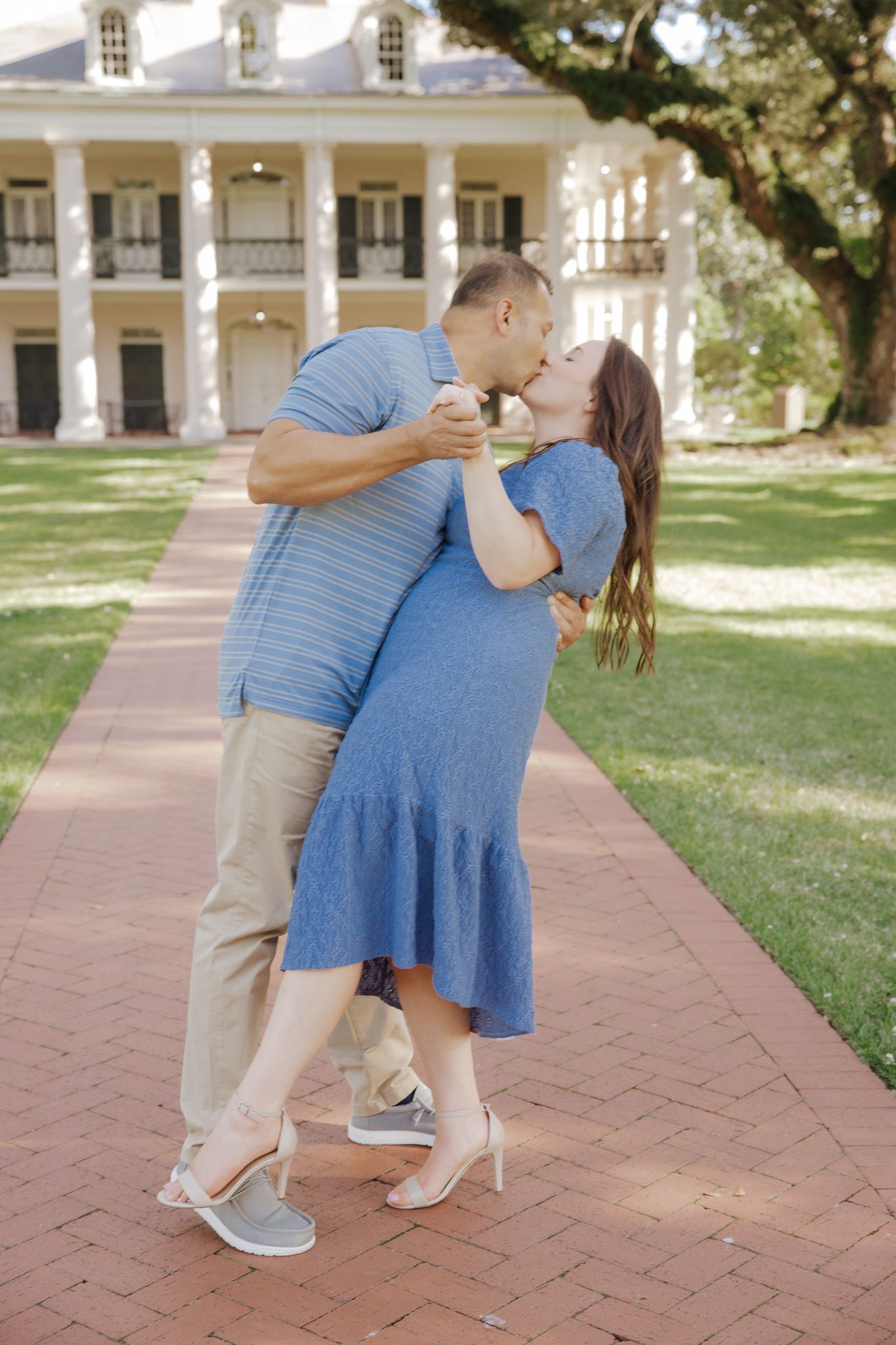 Couple sharing a romantic dip kiss on a brick path in front of a plantation home.