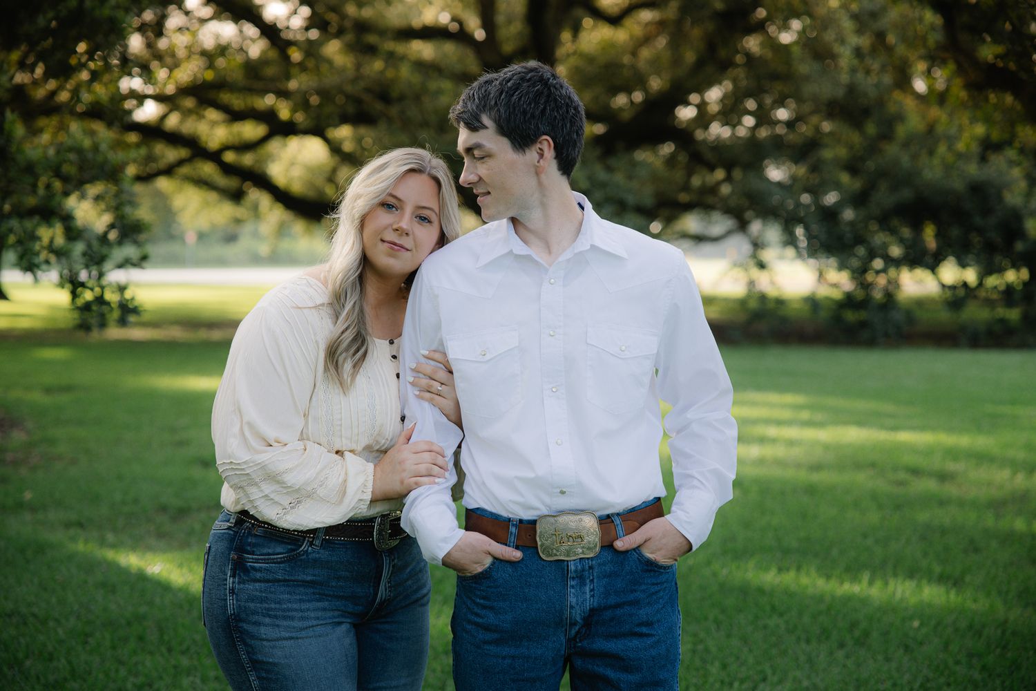 Young couple shares a tender moment outdoors under sprawling oak trees during an engagement photo session.