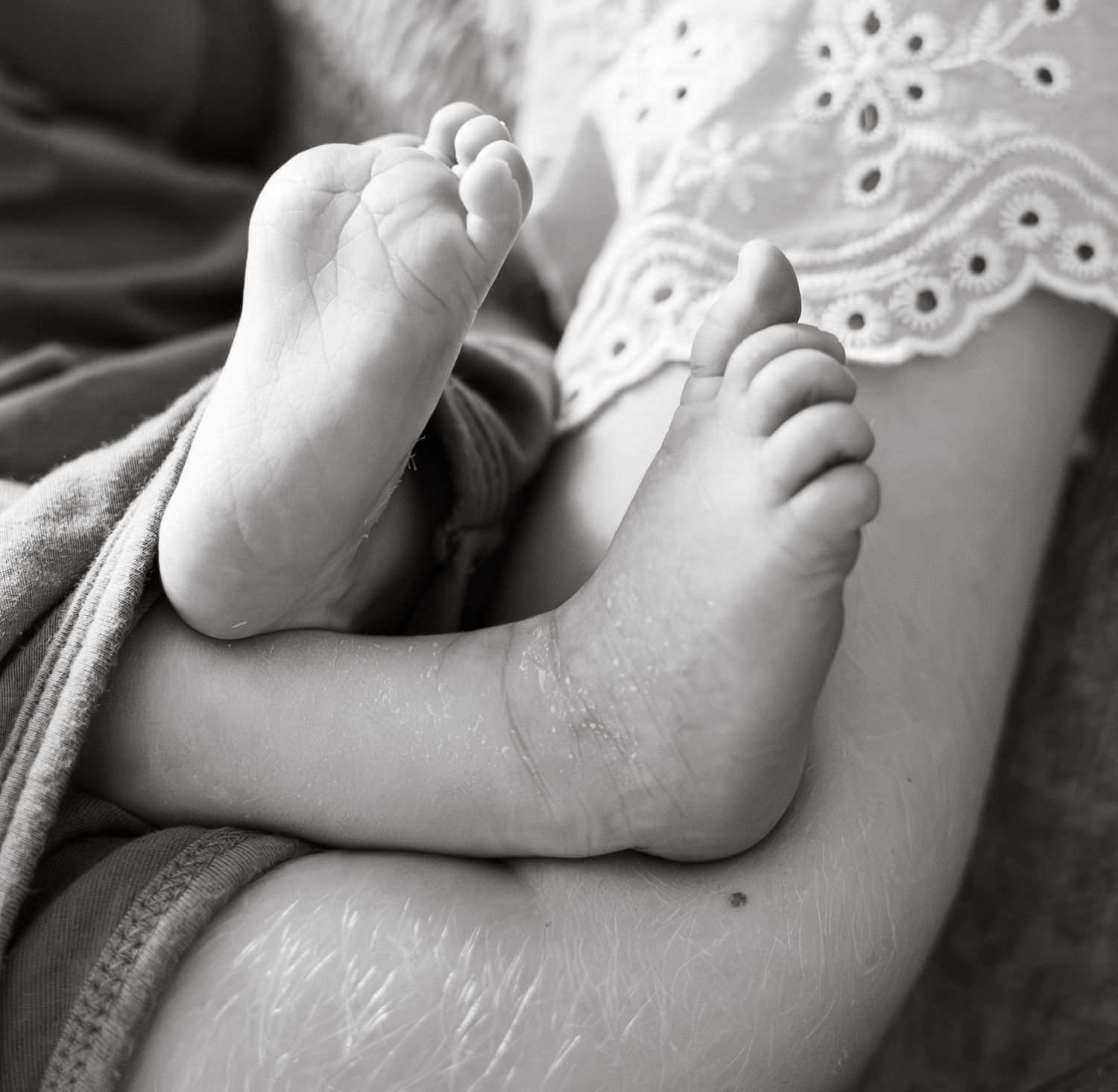 Black and white macro photo of delicate newborn baby feet with lace fabric detail.