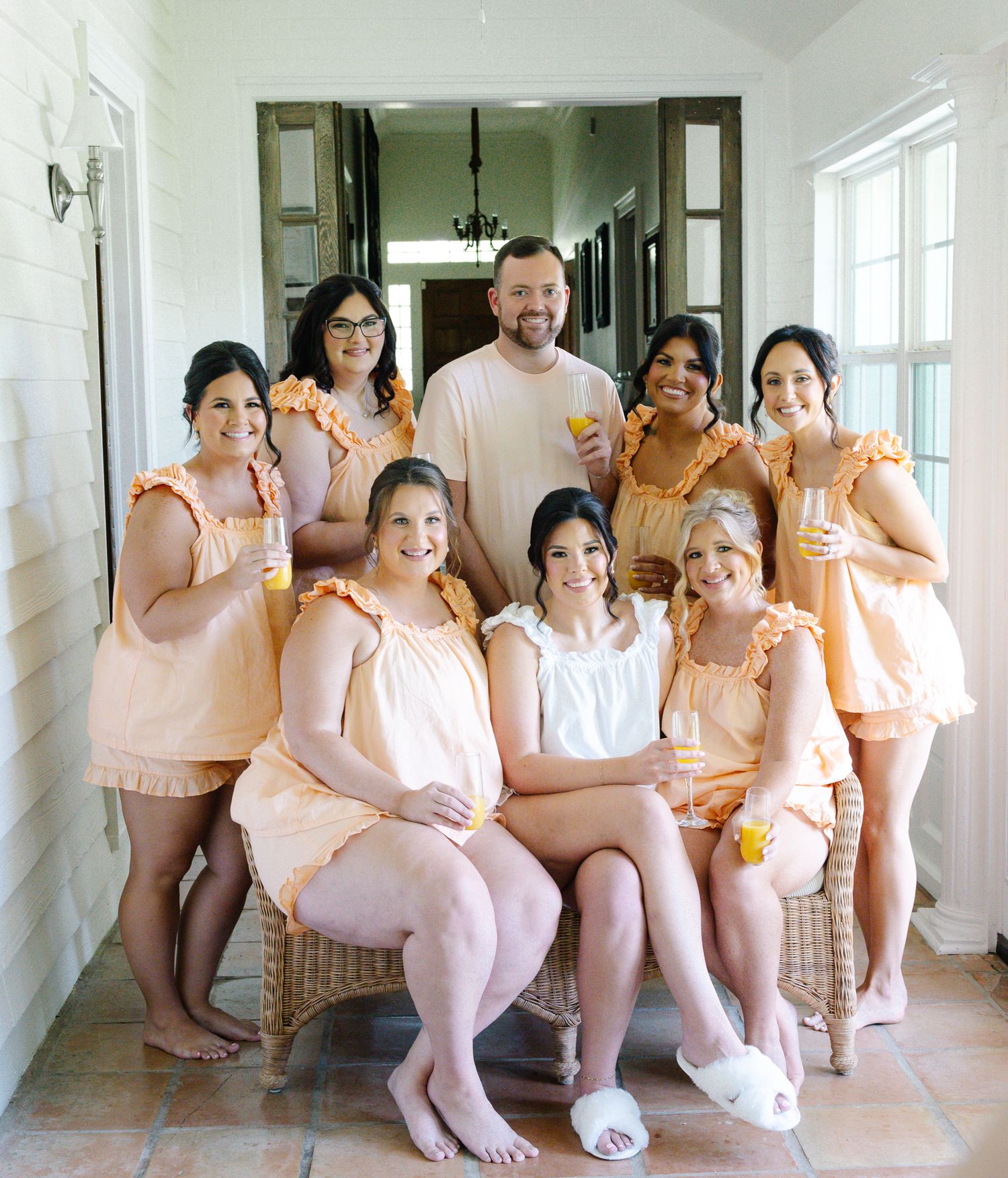 Bride poses with bridesmaids and hairstylist in matching peach ruffle sets during wedding morning prep.