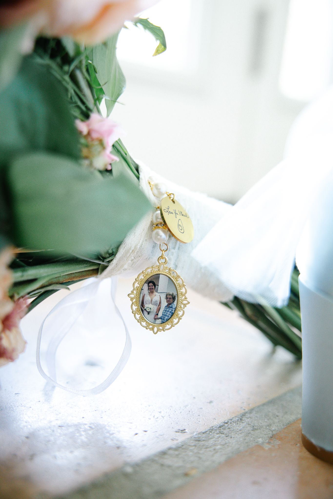 Close-up of a bridal bouquet charm featuring a vintage photo pendant and gold monogram tag.