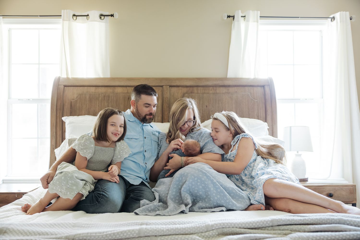 Joyful family of five cuddling together on a large bed with their newborn baby boy.