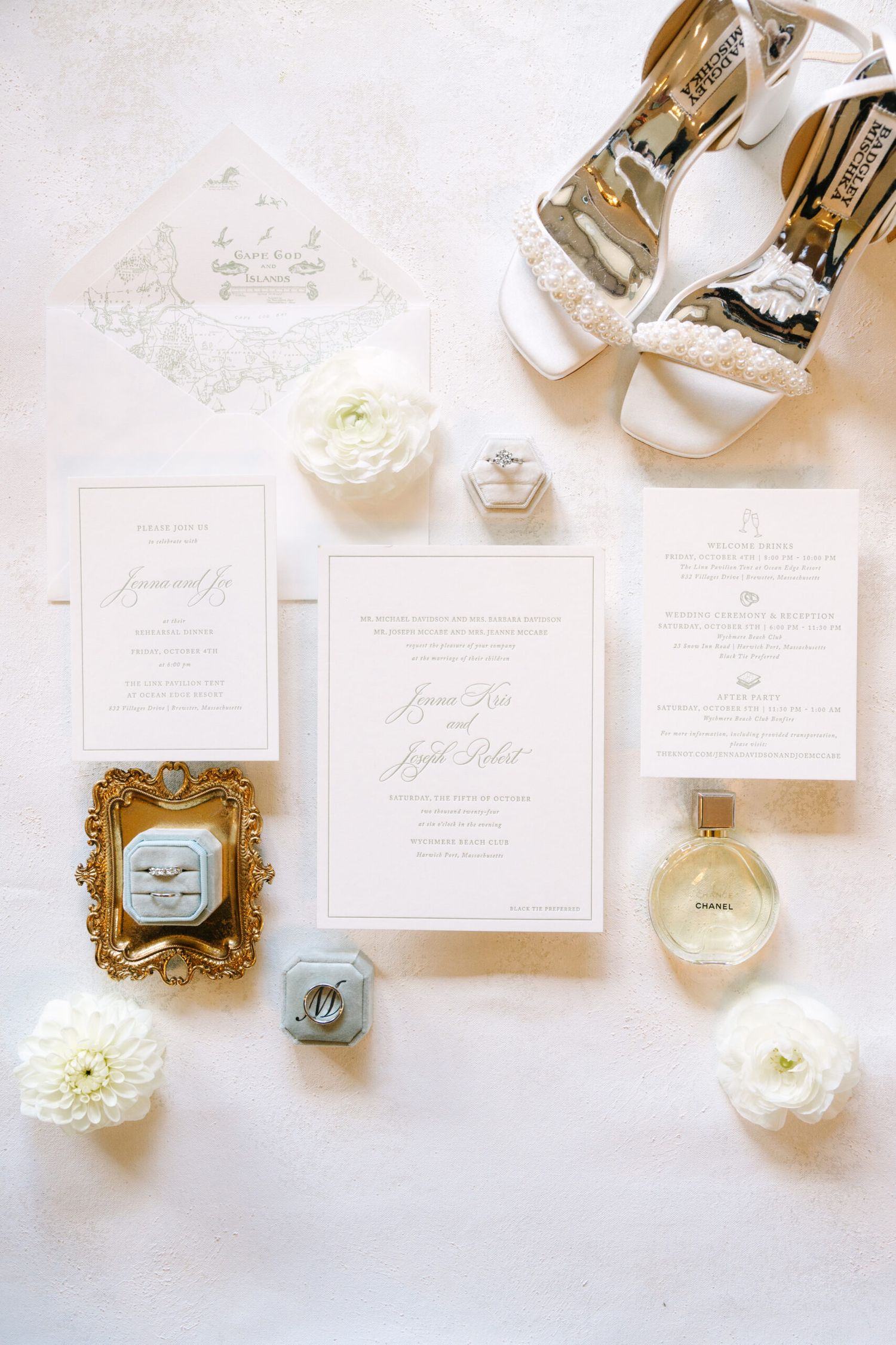 Classic white wedding invitation suite flat lay with gold frame, ring boxes, Chanel perfume, and white flowers.