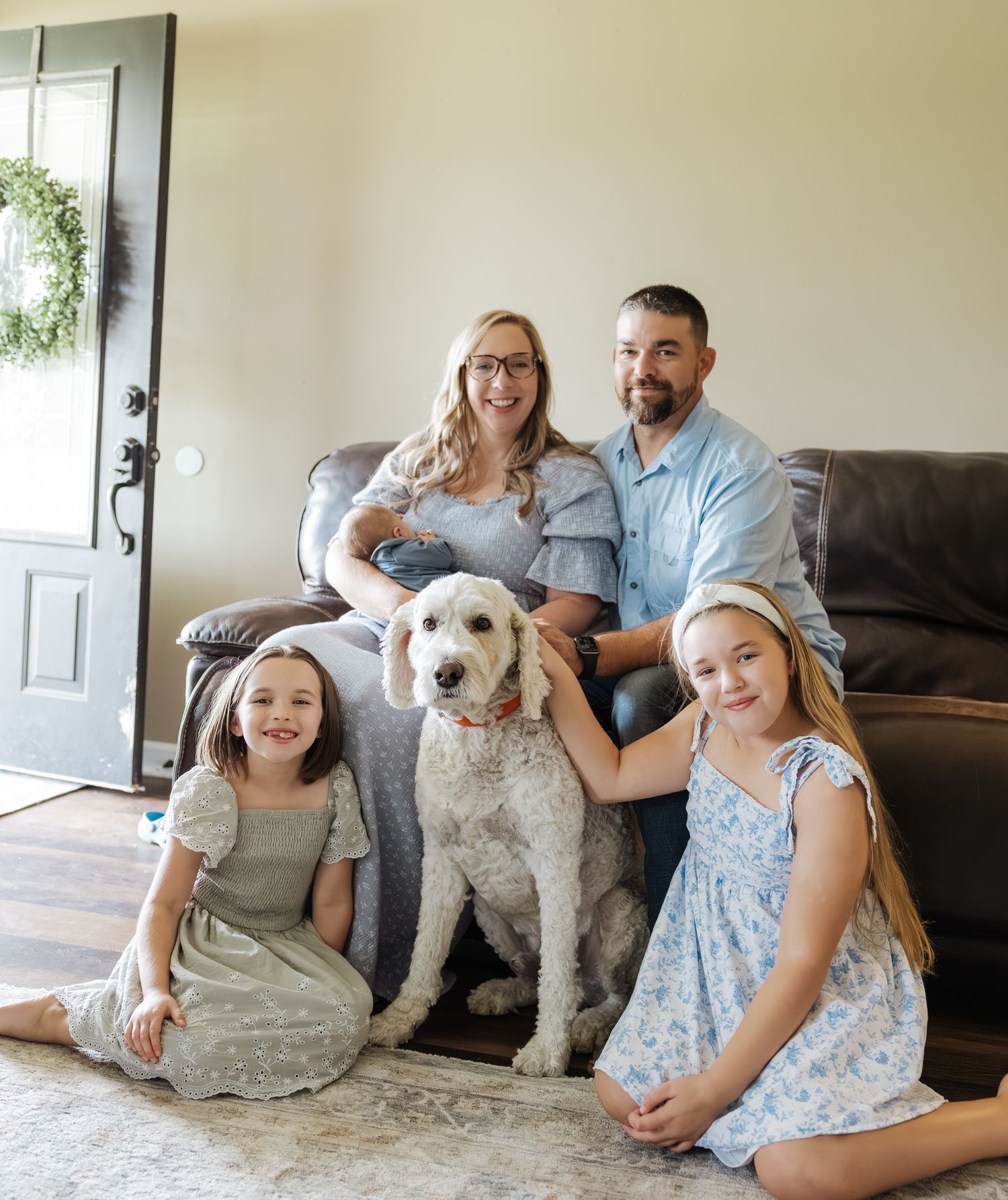 A happy family of four with a white dog poses together in their living room for a portrait.