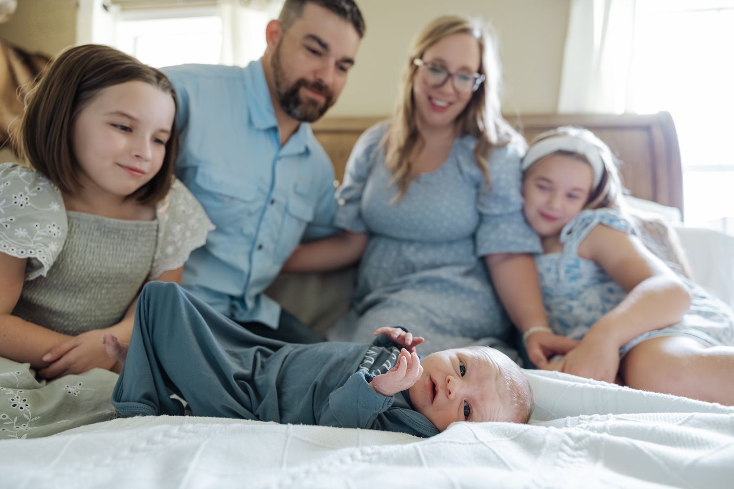 Family of five on a bed smiling as newborn baby Lucas lies on his back looking up.