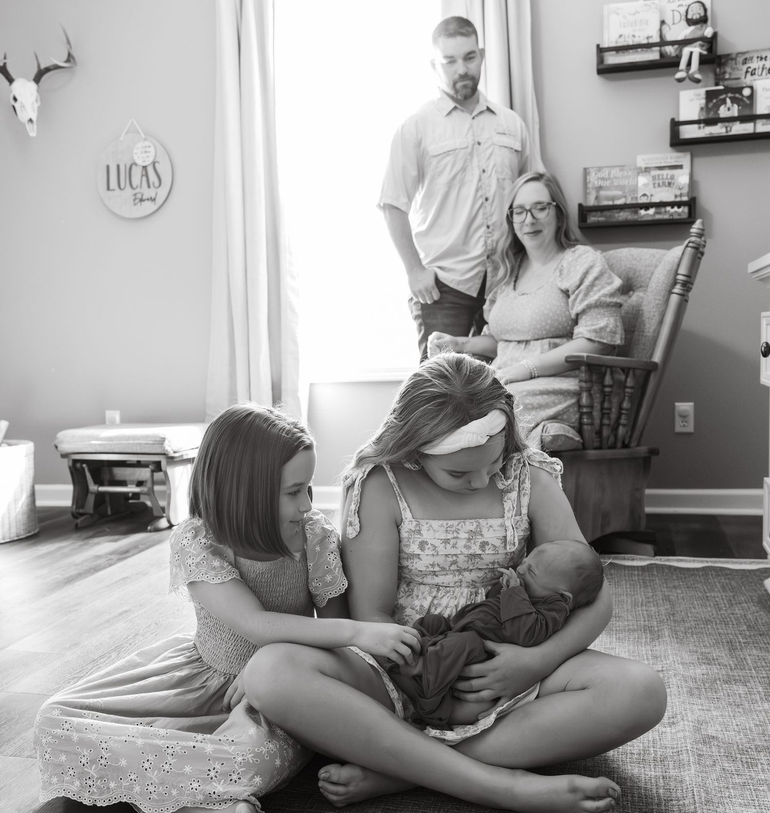 Black and white photo of family gathered around older sister holding newborn baby.