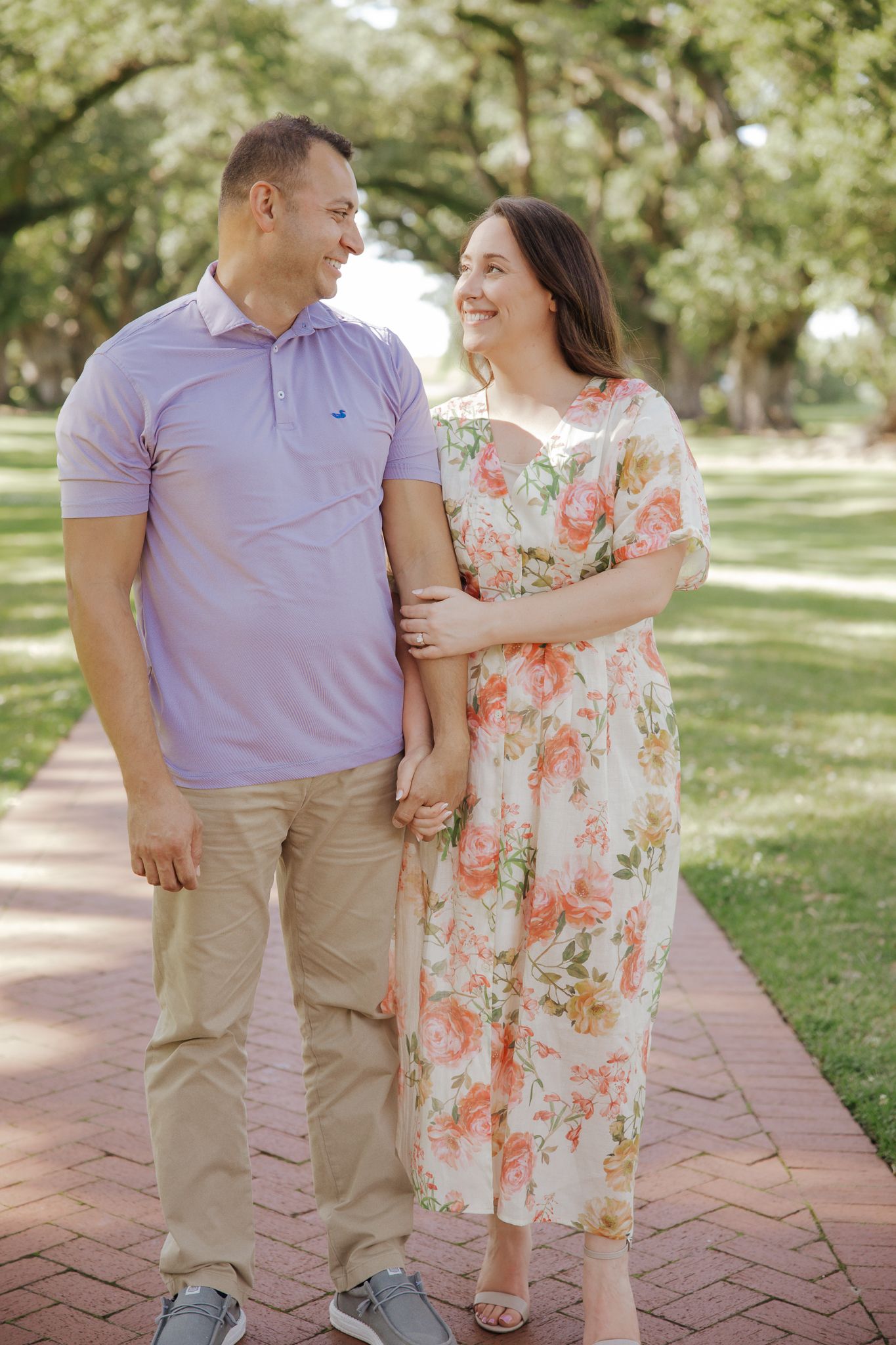Happy couple walking arm in arm on a brick path lined with oak trees.