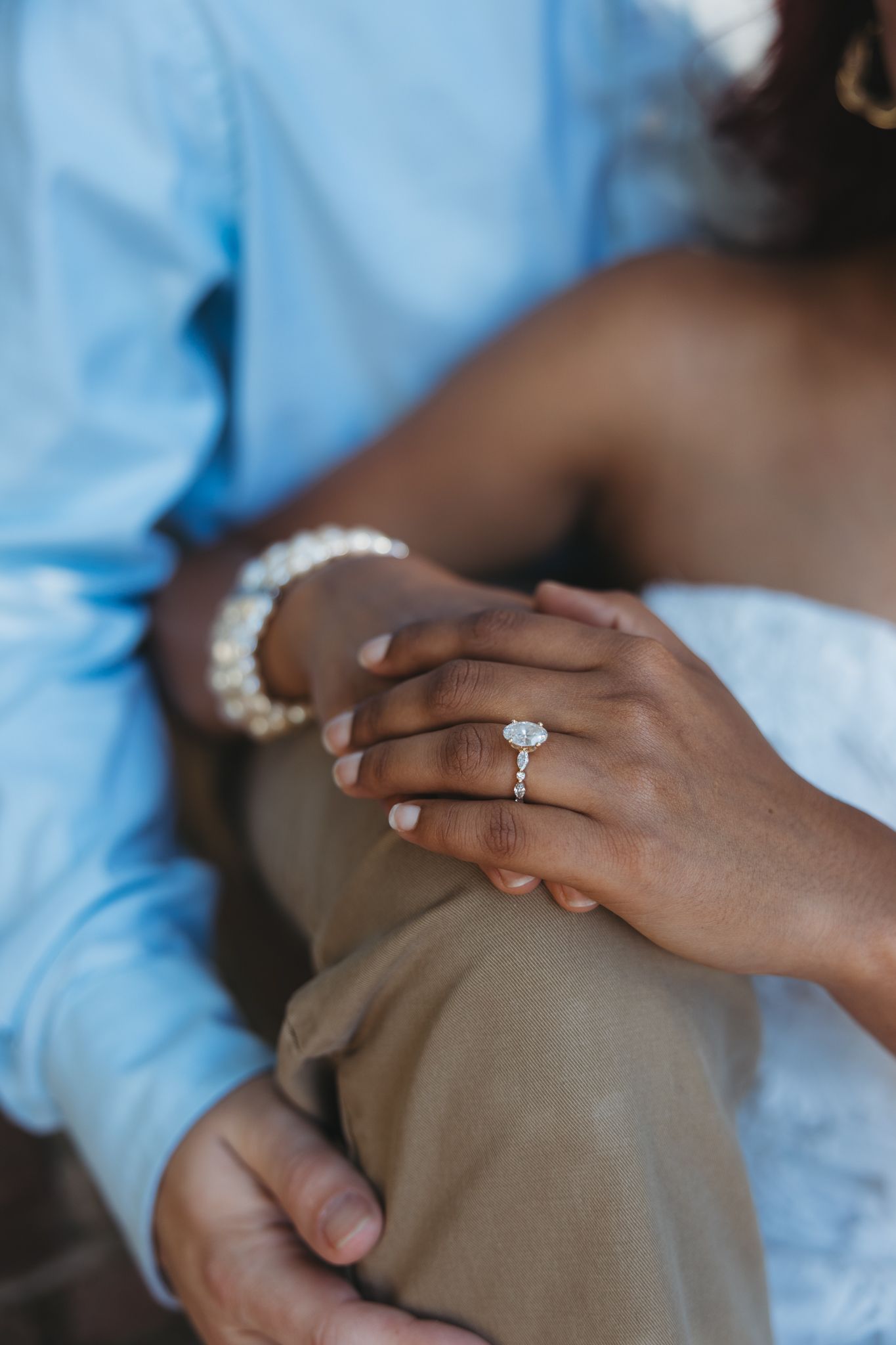 Close-up of a woman's hand adorned with a diamond engagement ring resting on a man's knee.