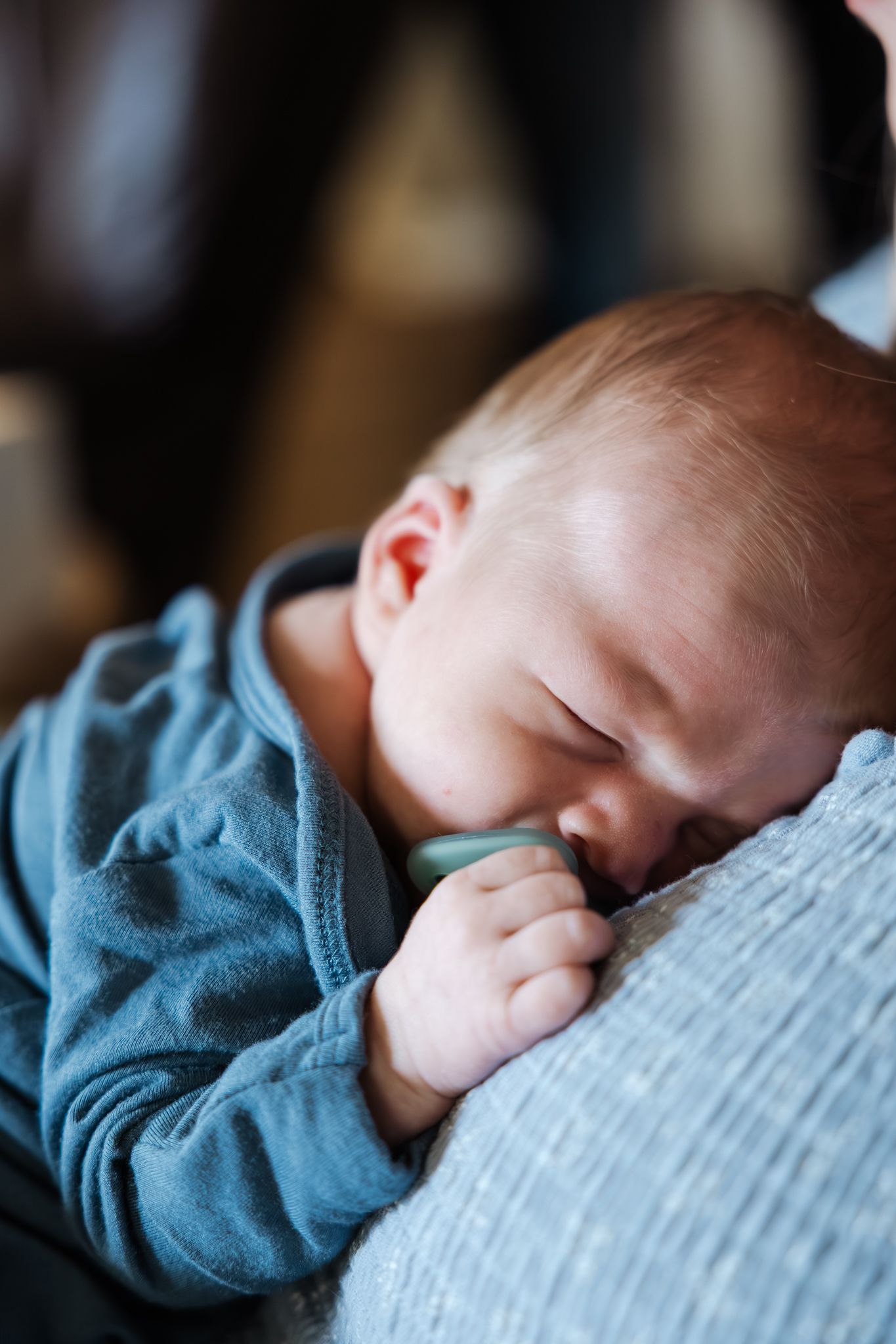A peaceful newborn baby in a blue sleeper rests their head on a soft blanket, eyes closed.