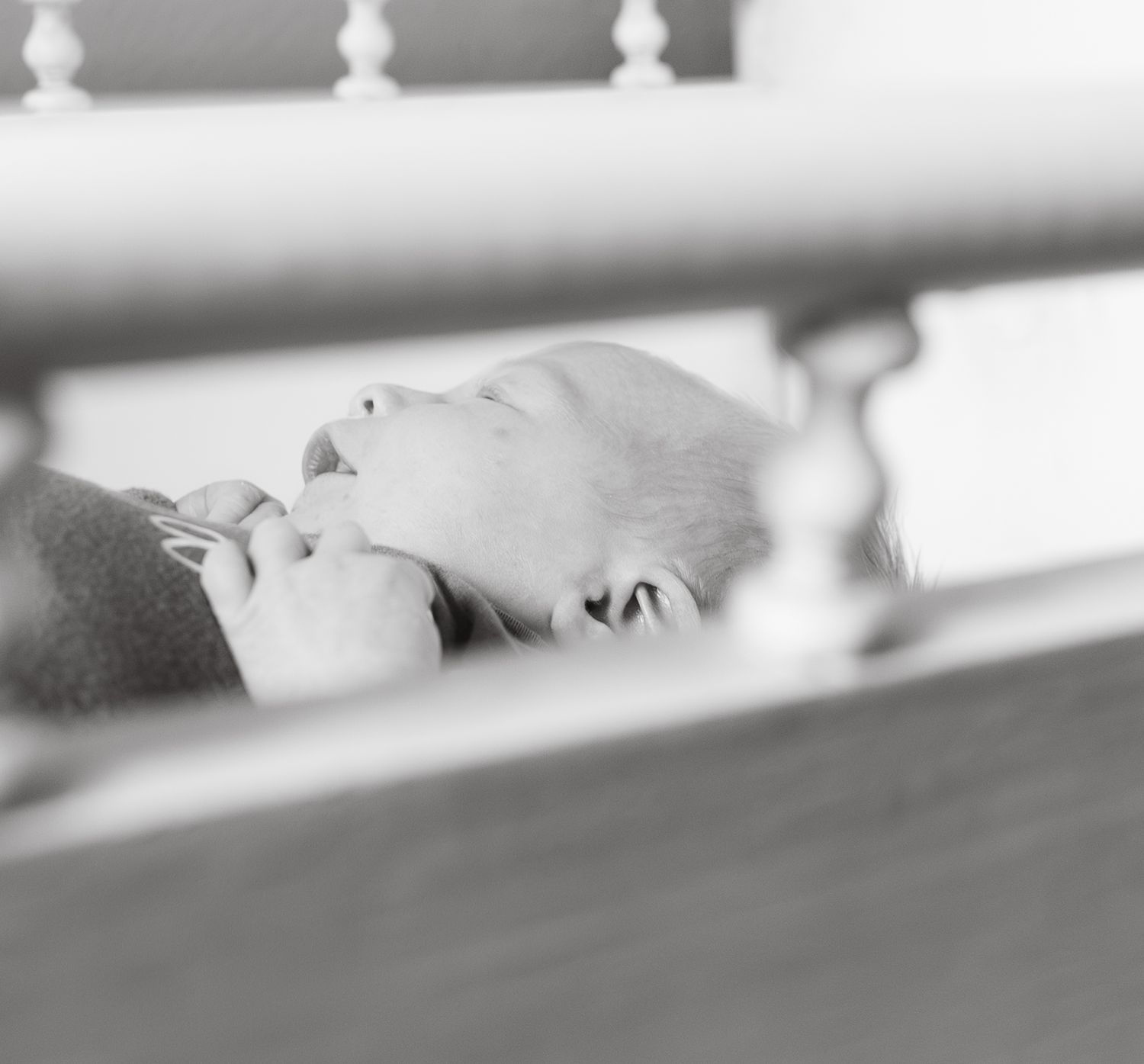 Black and white photo of a newborn baby being cradled and breastfed, viewed through wooden stair railings.