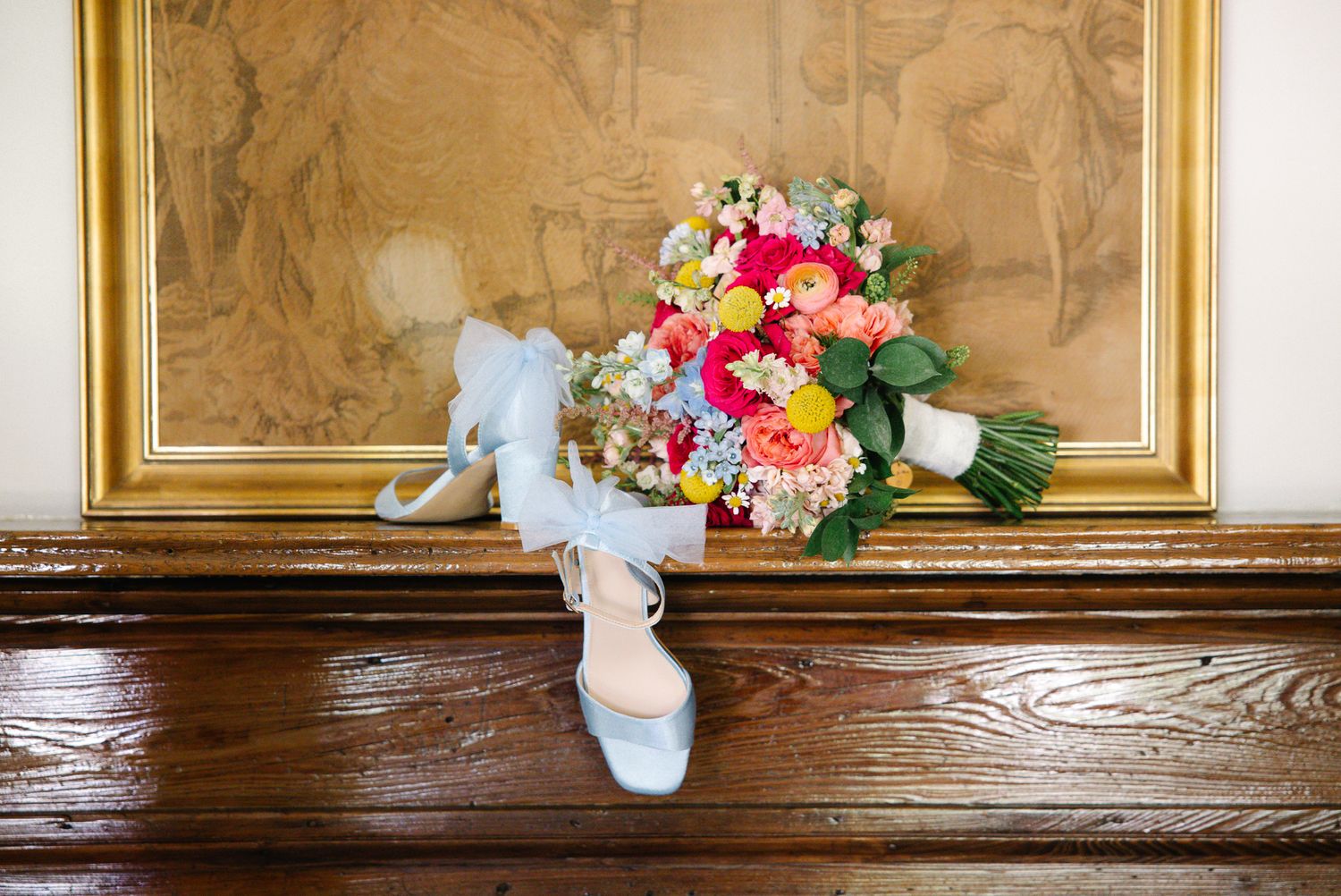 Vibrant bridal bouquet with bold mixed blooms displayed alongside light blue satin ankle-strap heels.