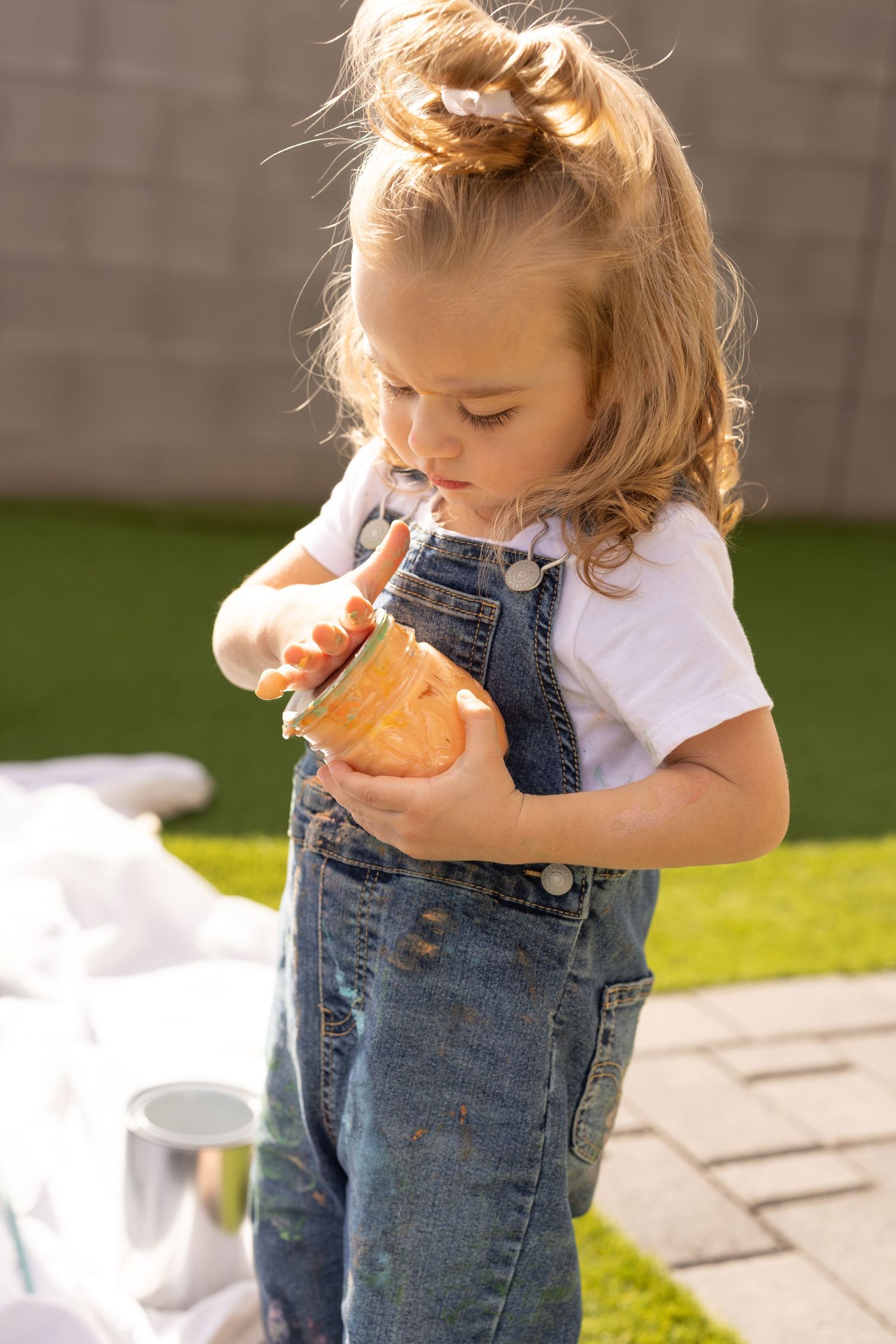 little girl playing with paint in denim overalls and white t-shirt