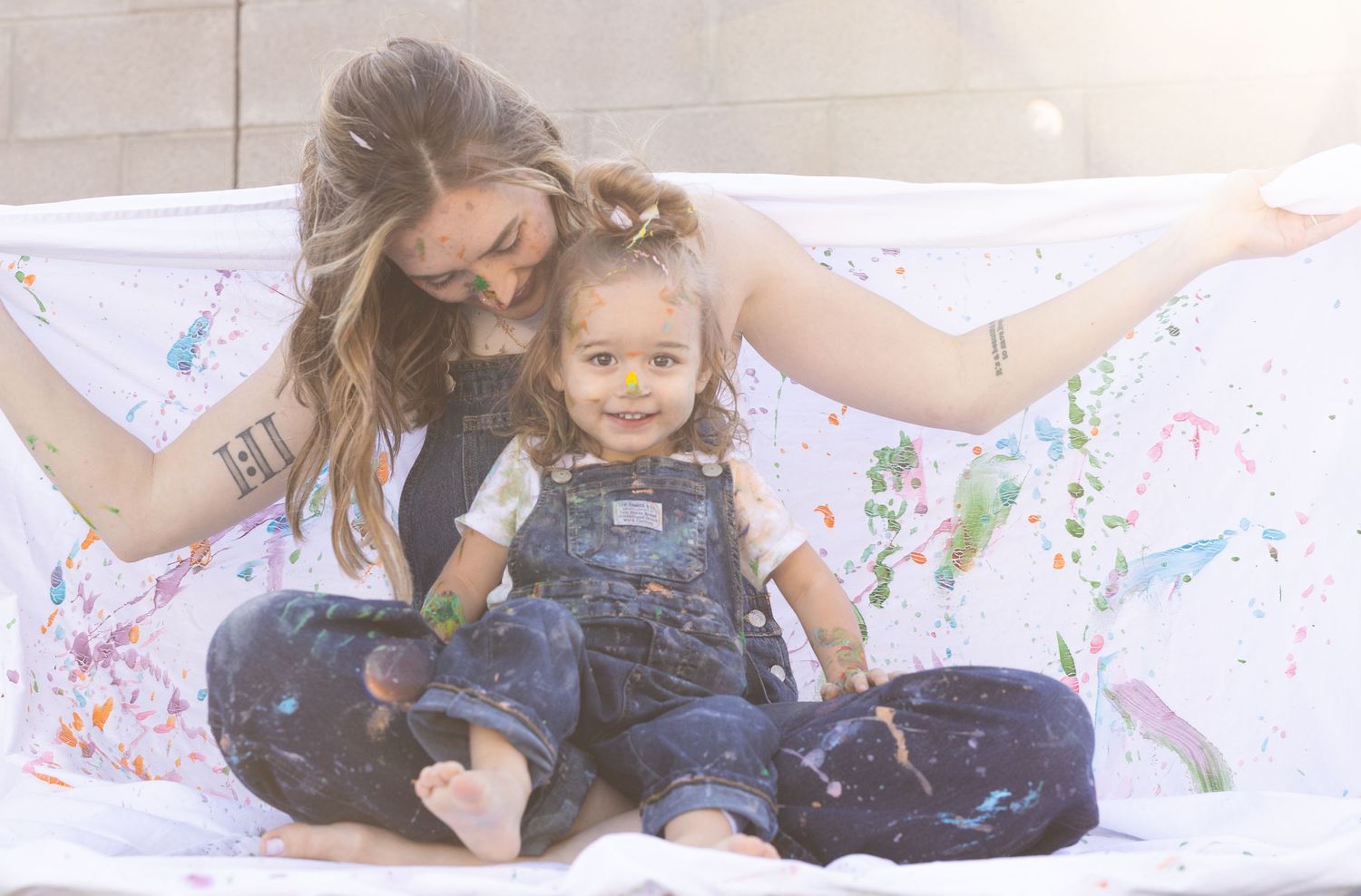 Mother holding daughter in a painting mommy and me photoshoot, denim overalls white t-shirt. backyard session Litchfield Park, Arizona