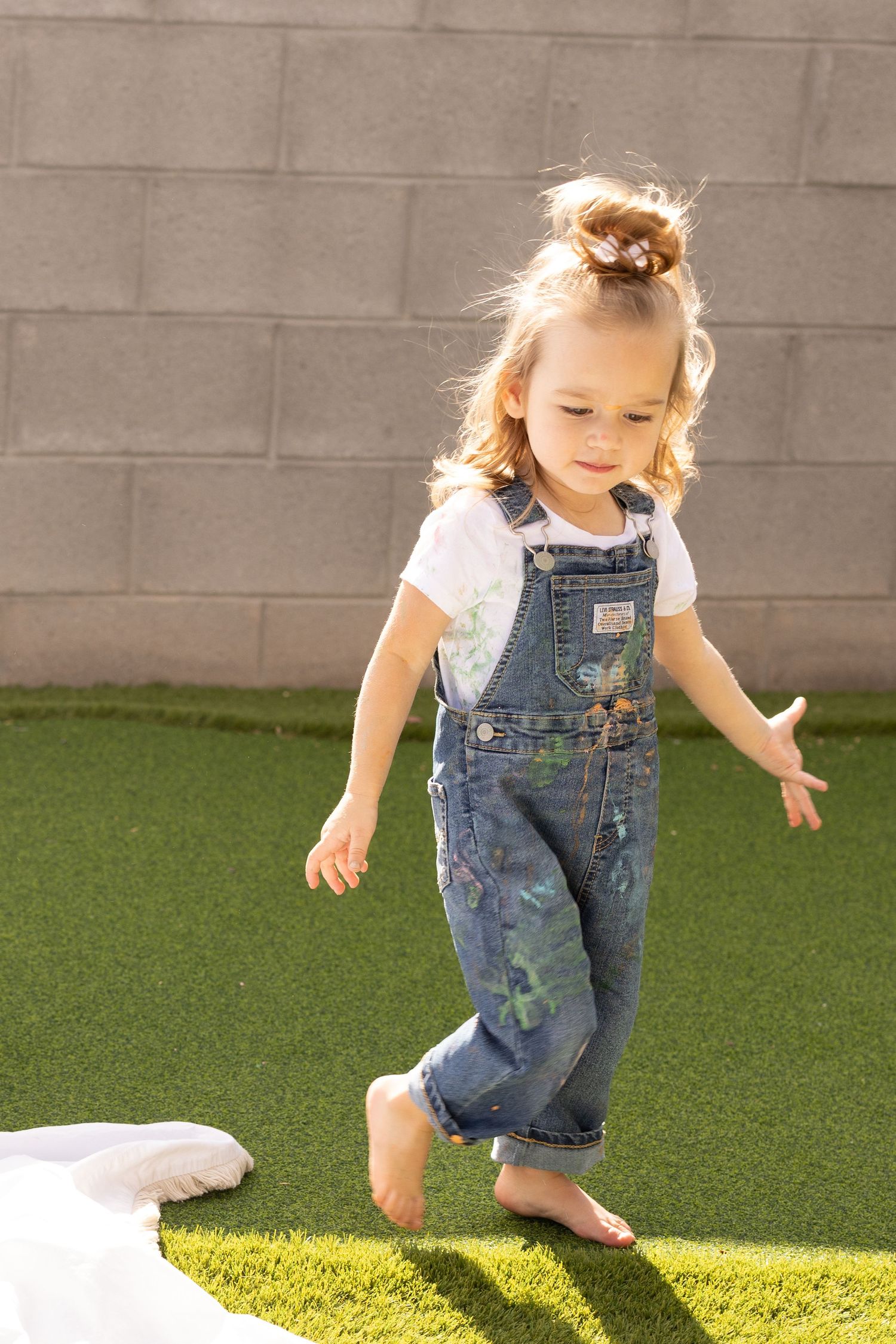 backlit photo of girl in denim overalls and white t-shirt during a mommy and me family photoshoot session. covered in color yogurt as paint