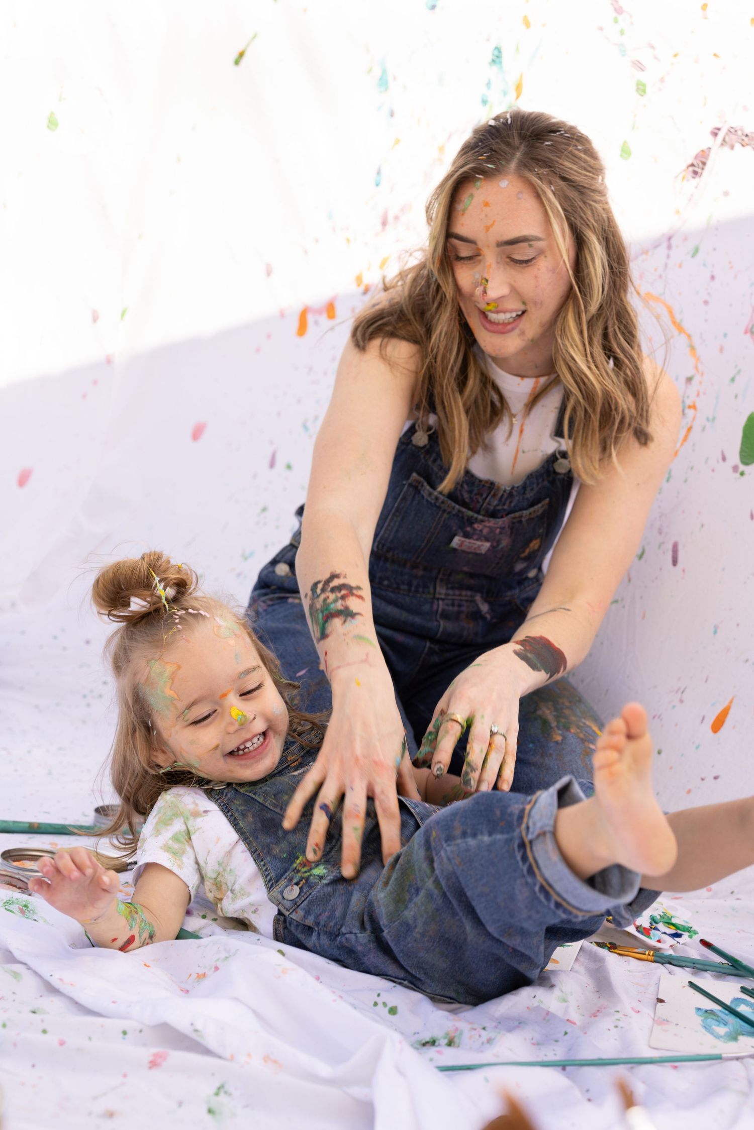 splatter paint mommy and me photoshoot, laughing child in denim overalls and white shirt