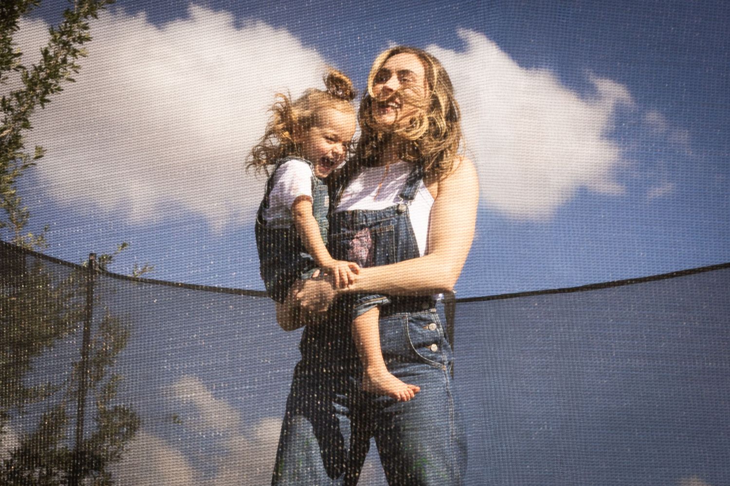 mother daughter jumping on trampoline, blue skies in background , smiling and happy