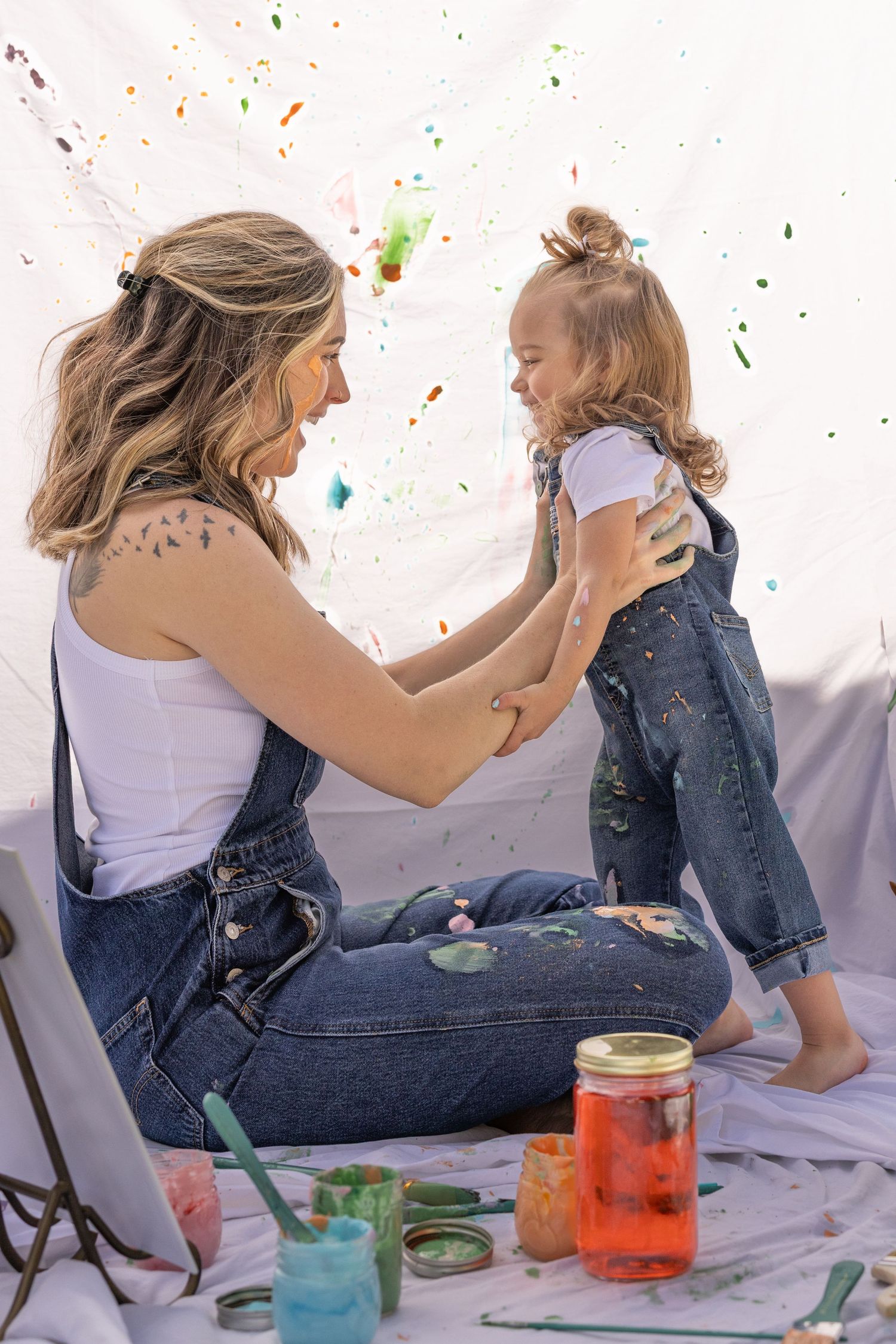 mother daughter holding daughter playfully tossing in air during a mommy and me photoshoot.  Outfit in white t-shirt and denim overalls