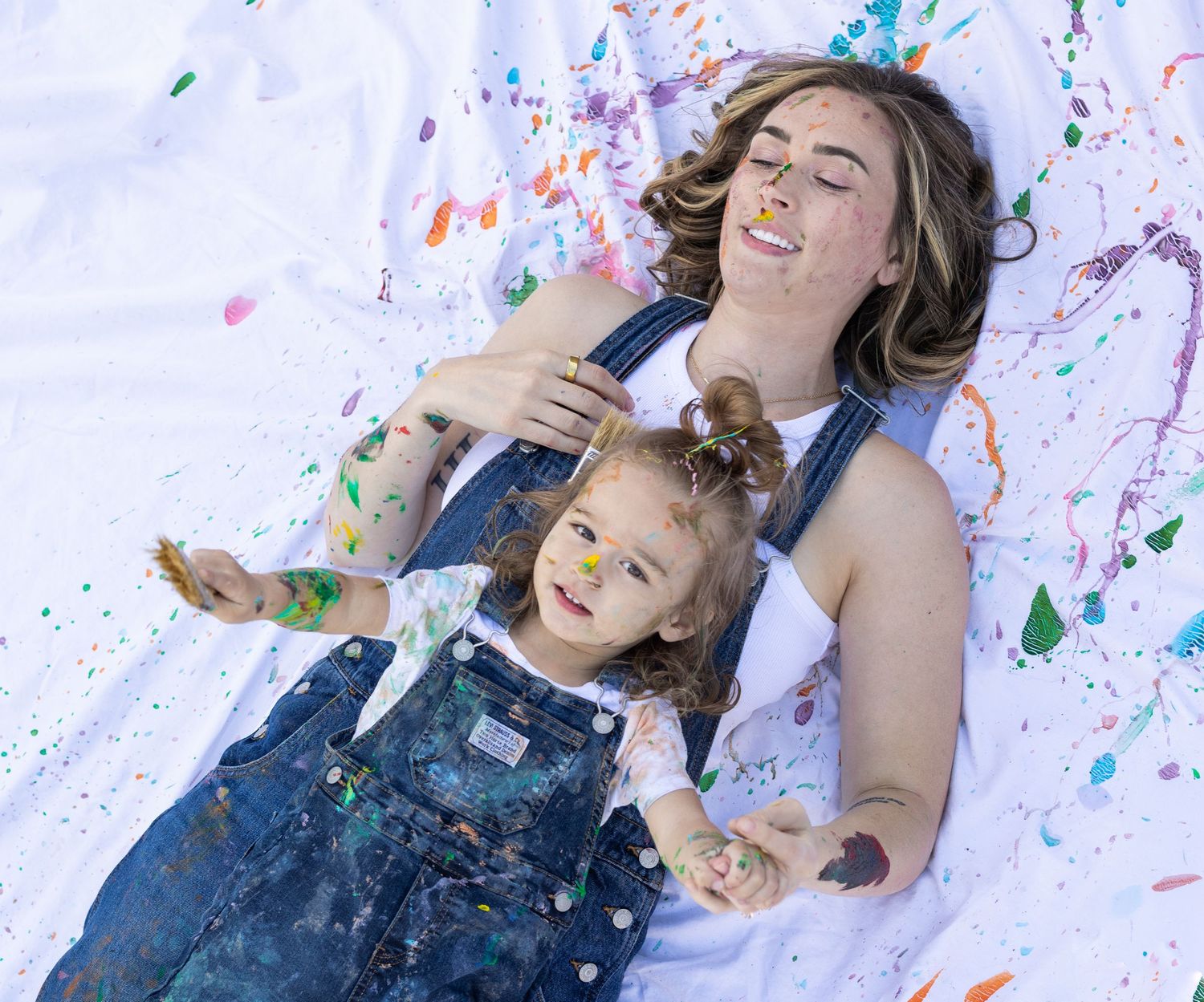 mother daughter mommy and me painting shoot, paying on paint covered sheet. mommy and me photoshoot.