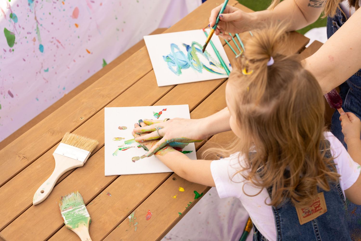 painting mother and daughter session. mommy and me photoshoot leaving hand prints on canvas over a mini picnic table.