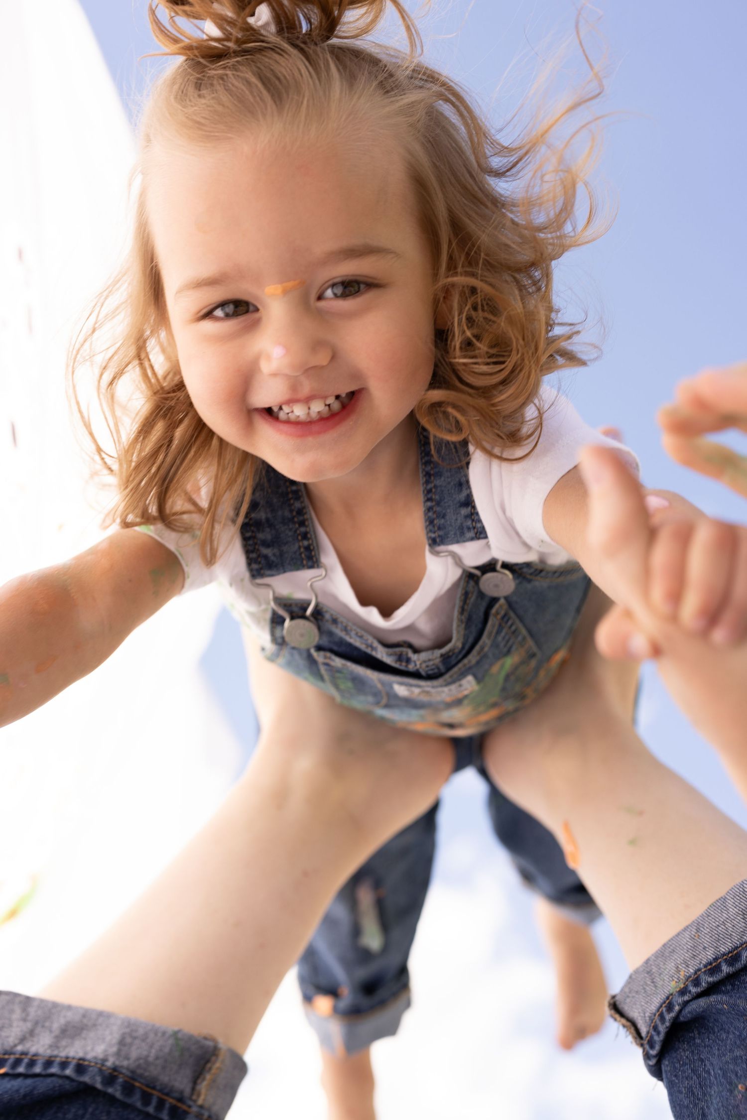 toddler being playfully tossed in the air by mother. covered in paint, sky in the background