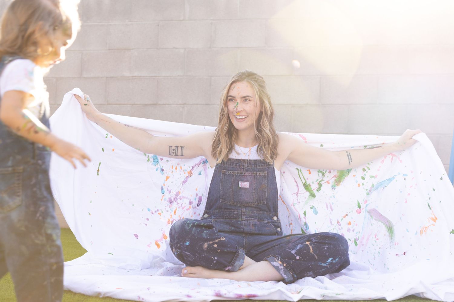 backlit photo sunflare in mommy and me photoshoot. covered in food colored yogurt used as non-toxic paint alternative. denim overalls