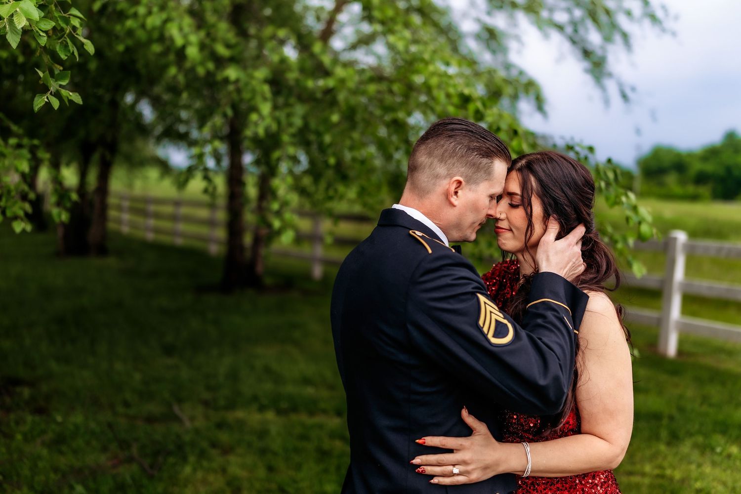 A couple in formal attire share a romantic moment outdoors, with the man in military dress uniform embracing a woman in a red gown.
