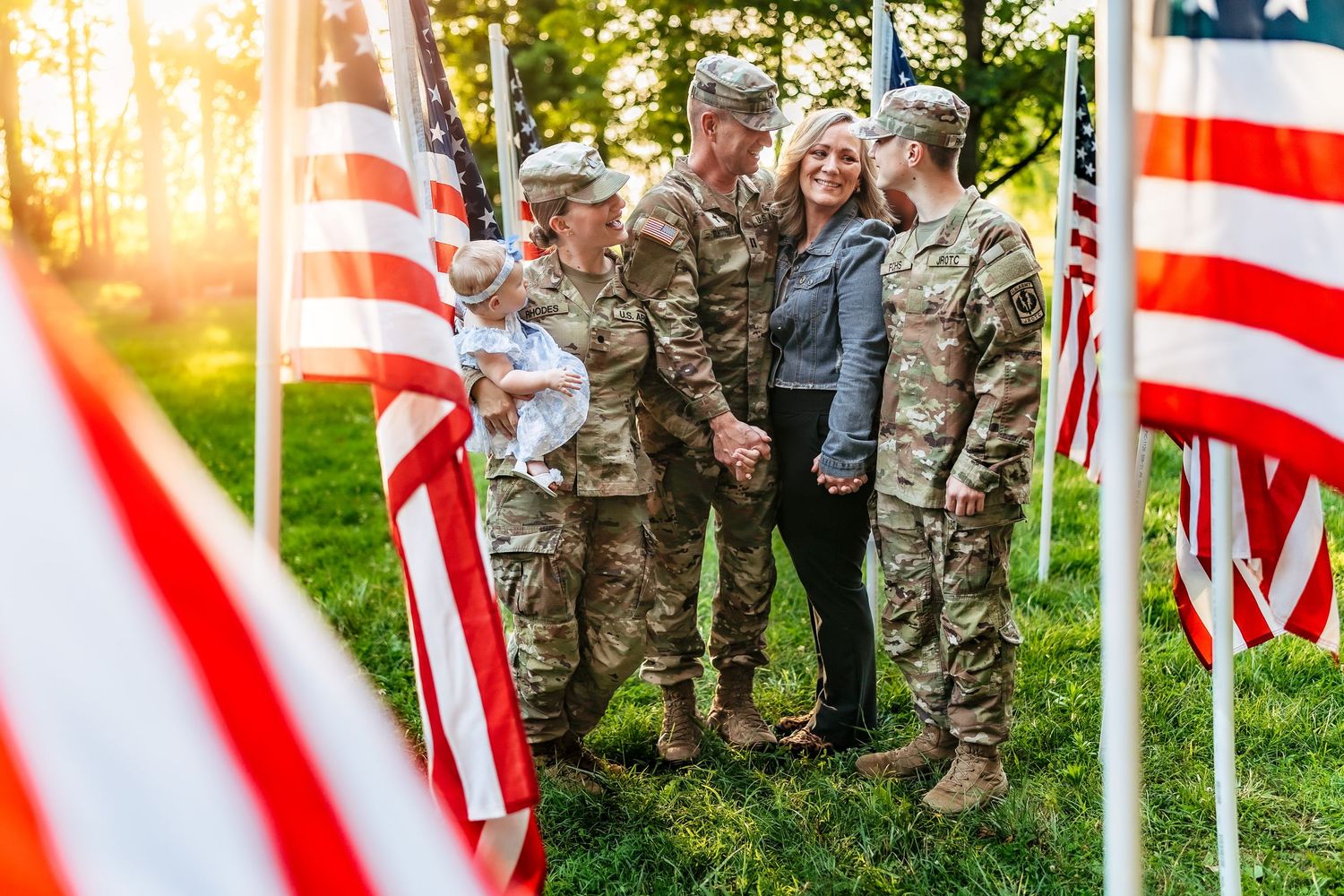Military family embracing among American flags at sunset in a heartfelt homecoming reunion outdoors.
