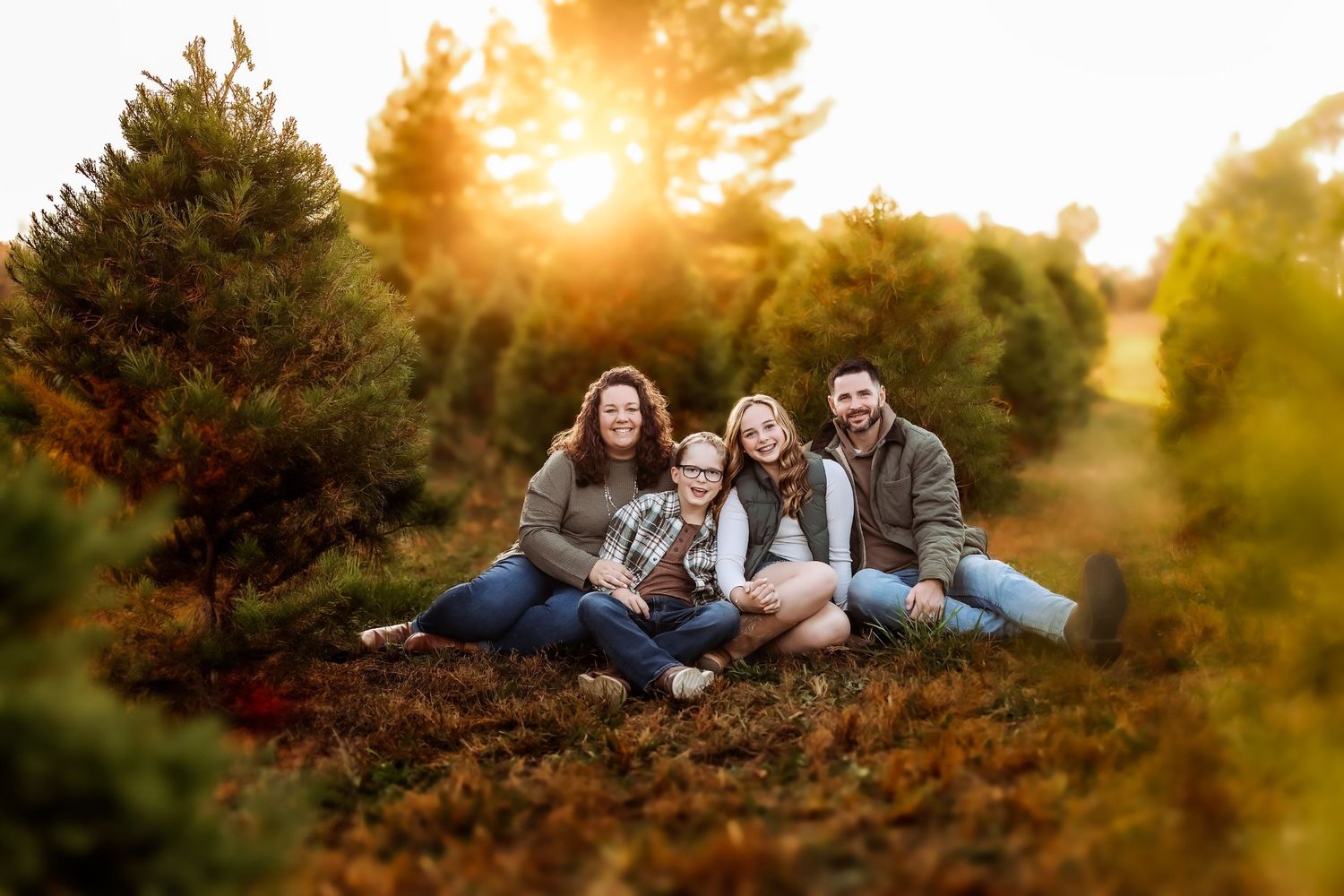 Family of four smiling together at a Christmas tree farm during golden hour sunset.