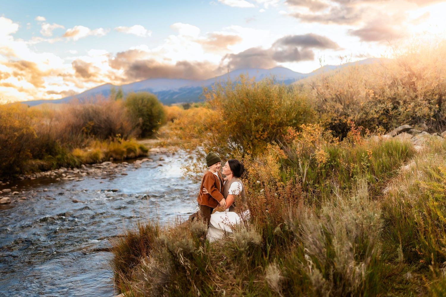 Couple kissing by a mountain stream surrounded by autumn foliage at golden hour sunset.