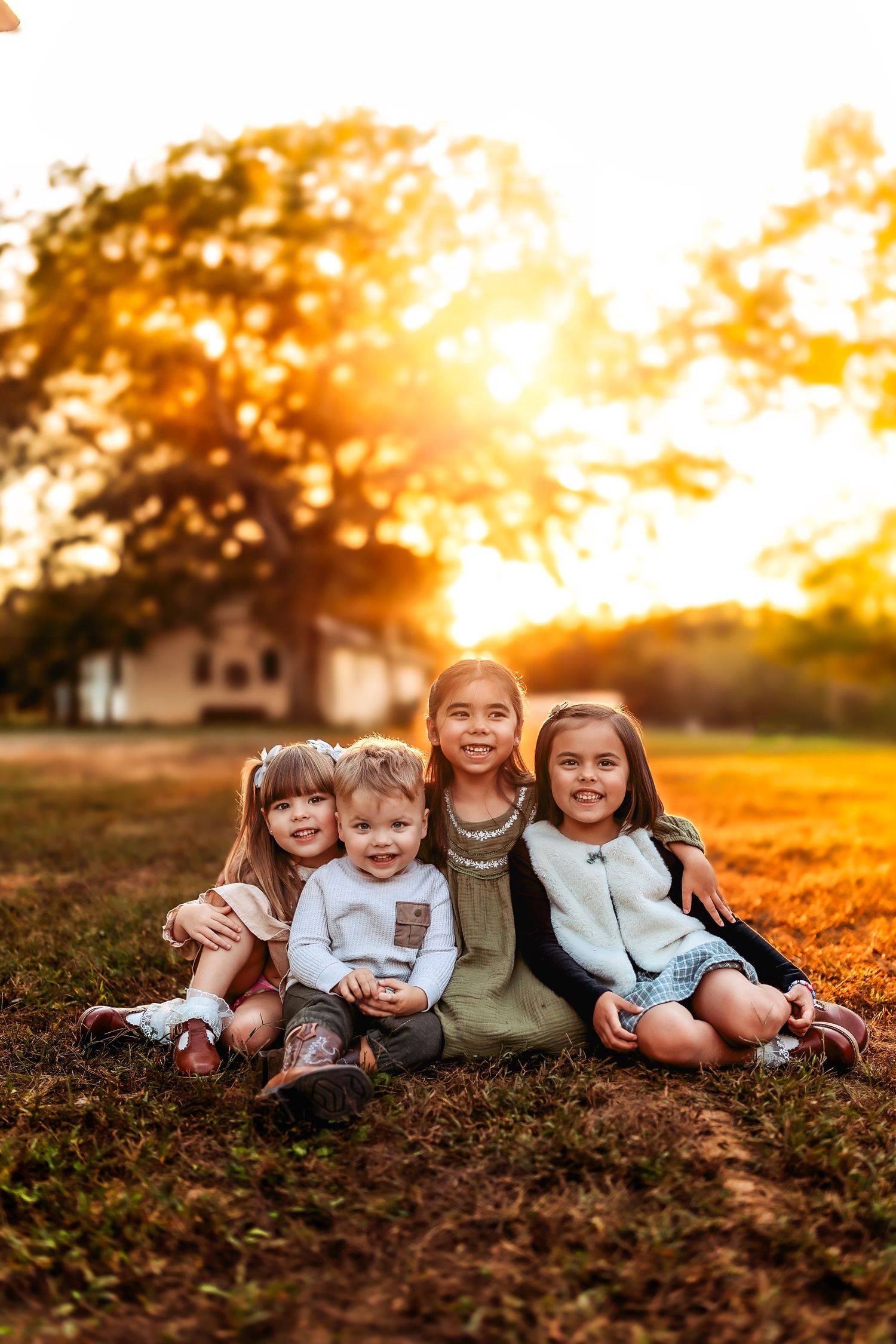 Four young children sitting together on grass during golden hour sunset in a park.
