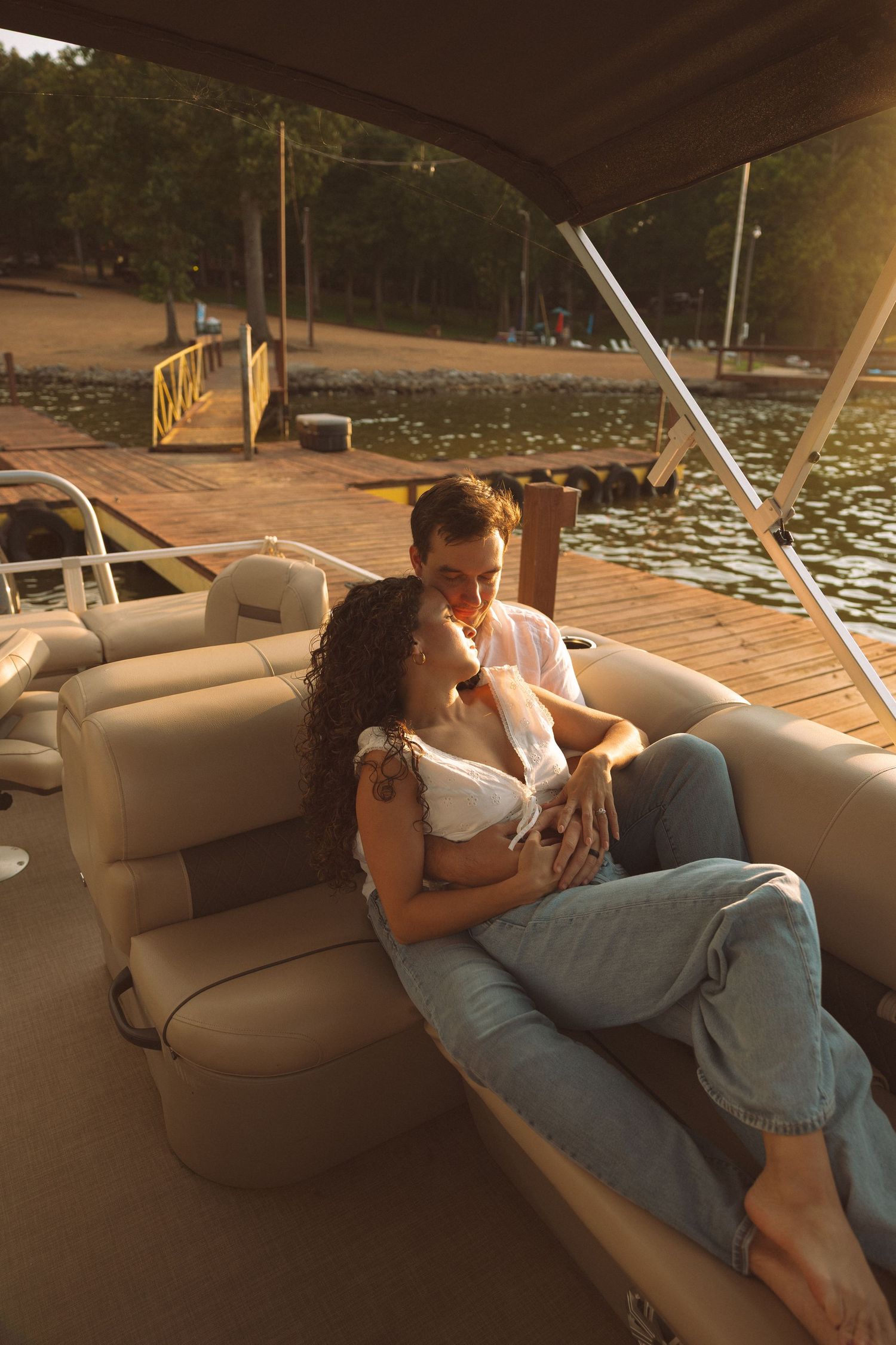 Romantic couple cuddling on a pontoon boat near a wooden dock during golden hour sunset.