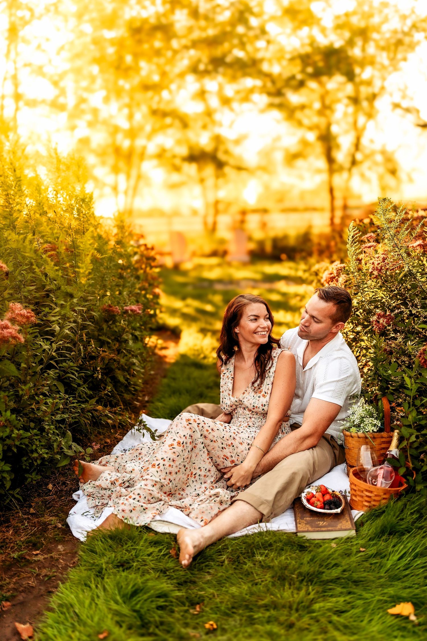 Romantic couple enjoying a sunset picnic on green grass surrounded by lush garden flowers and warm golden light.