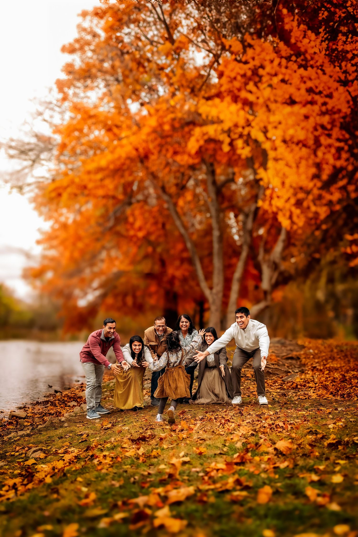 Group of friends posing playfully by a river surrounded by vibrant orange autumn foliage on a fall day.