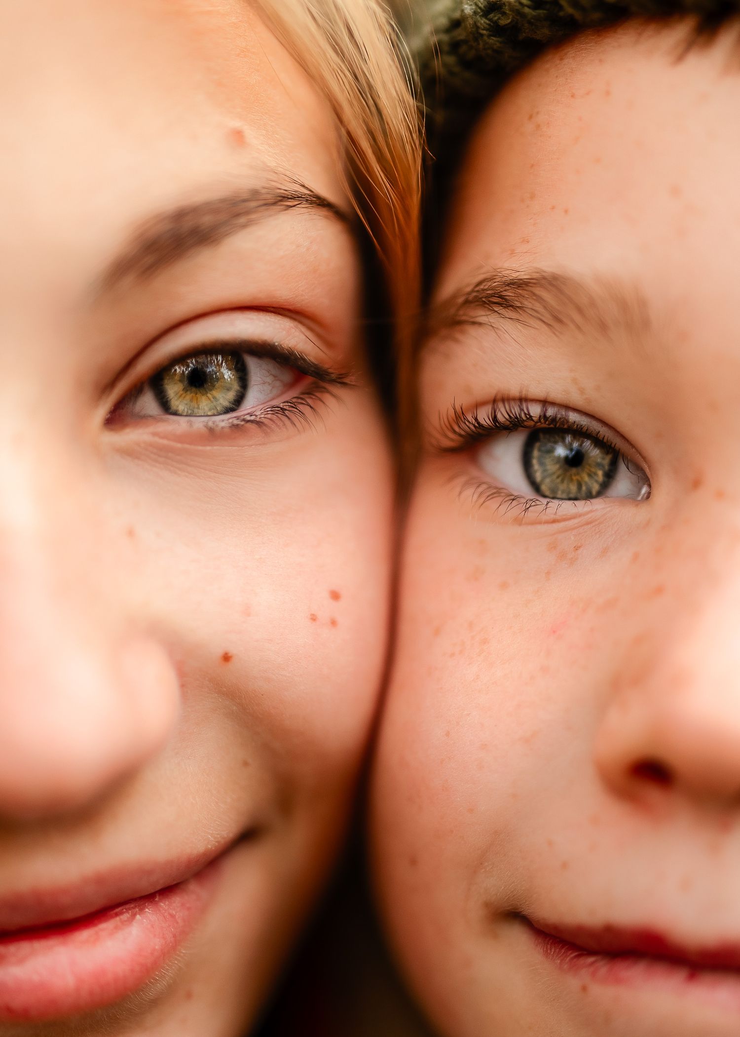 Close-up portrait of two children with striking green eyes and freckles pressing their faces together.