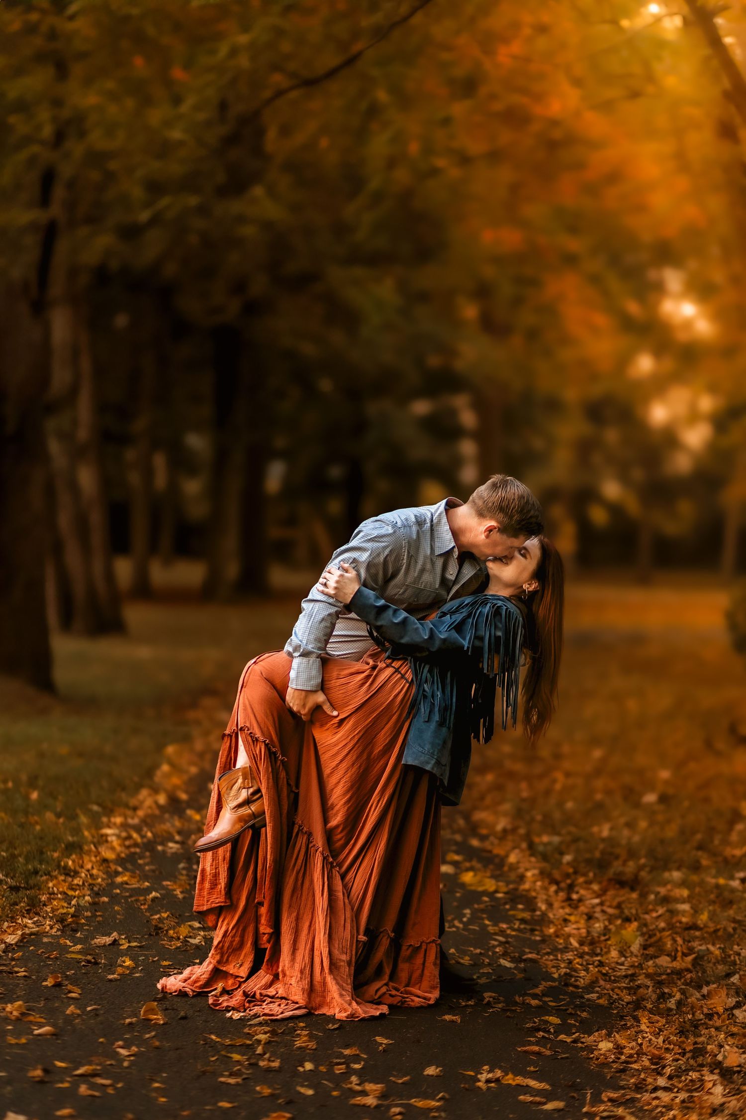 Couple sharing a romantic dip kiss on an autumn park path surrounded by golden fall foliage.
