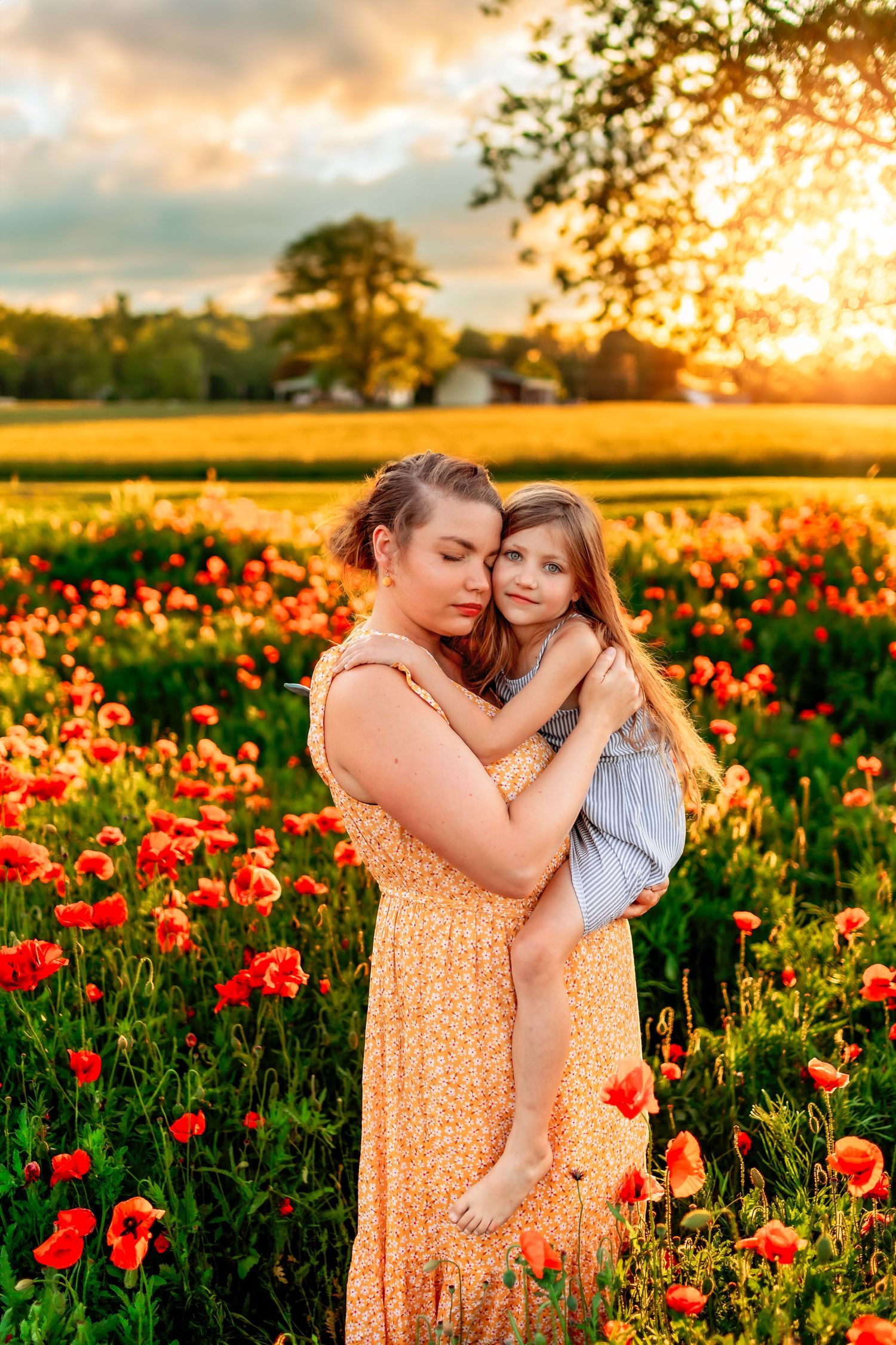Mother holding daughter in a sunlit poppy field at golden hour, both in summer dresses, surrounded by red blooms.