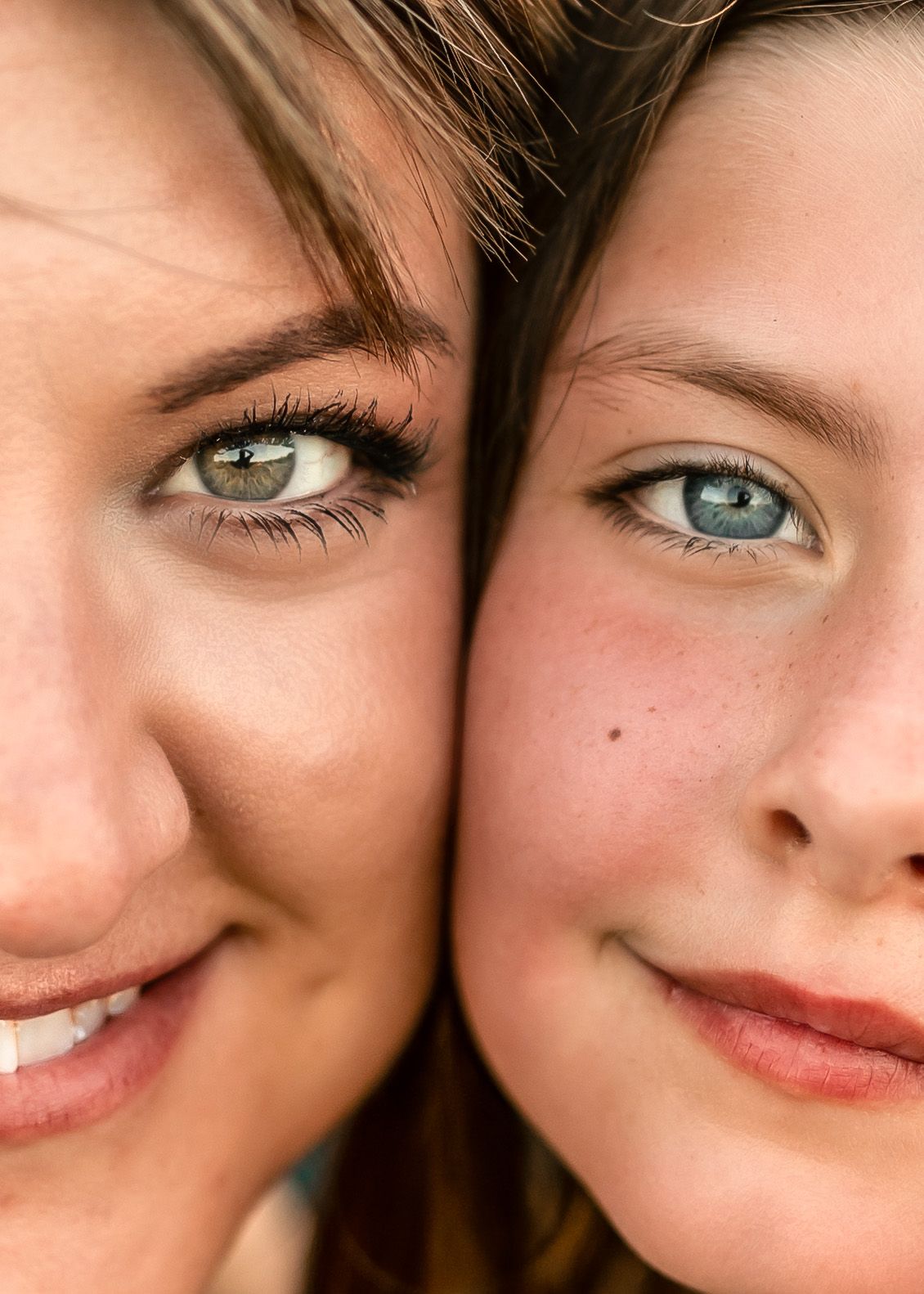 Close-up portrait of two women with blue-green eyes and brown hair posing cheek to cheek, smiling softly.