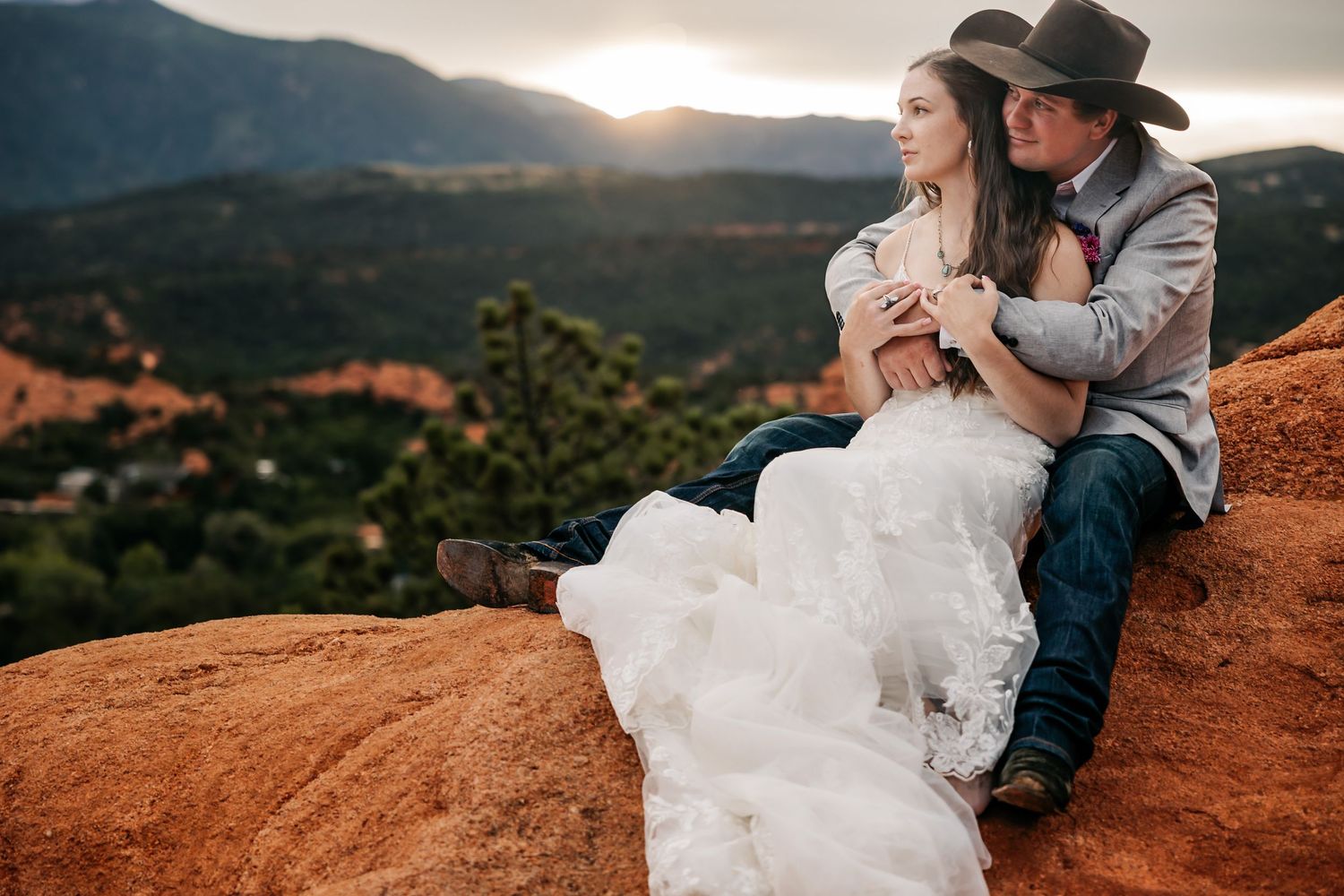 Couple in western attire sitting on red rocks at sunset with mountain views at Garden of the Gods.