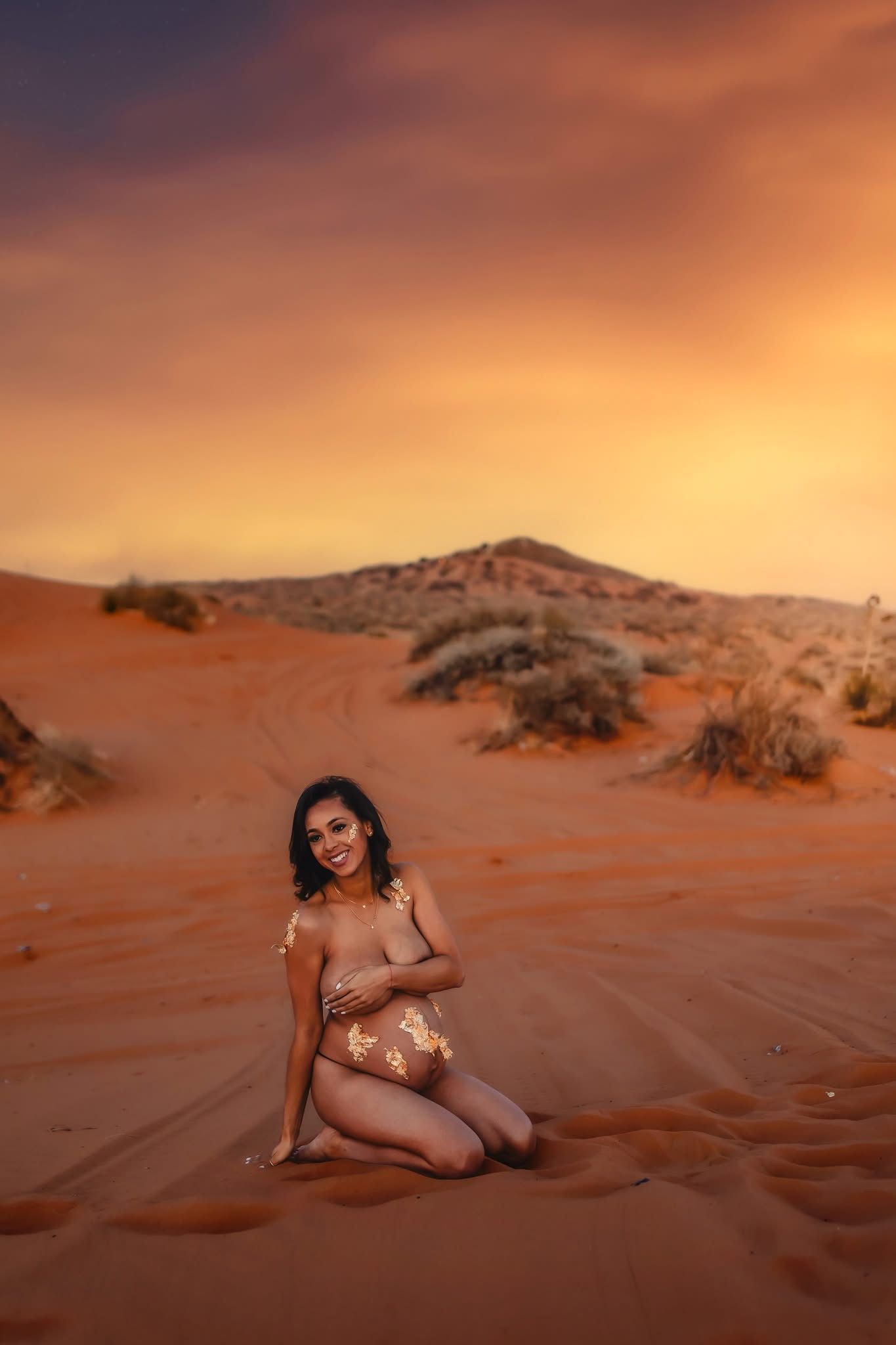 Woman posing on red sand dunes at sunset in a desert landscape with dramatic orange sky.