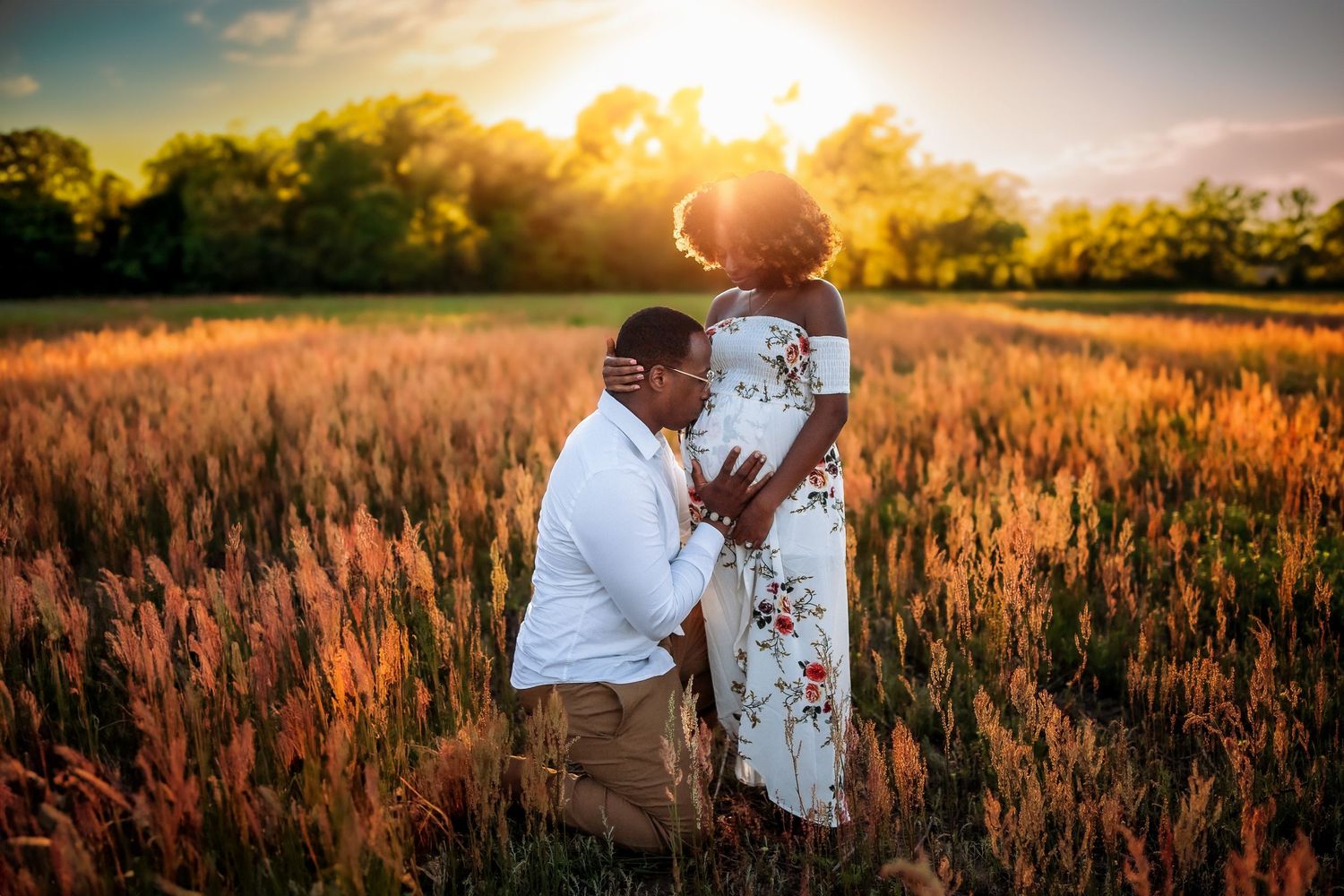 Couple sharing a romantic moment in a golden field at sunset, man kneeling before woman in floral dress.