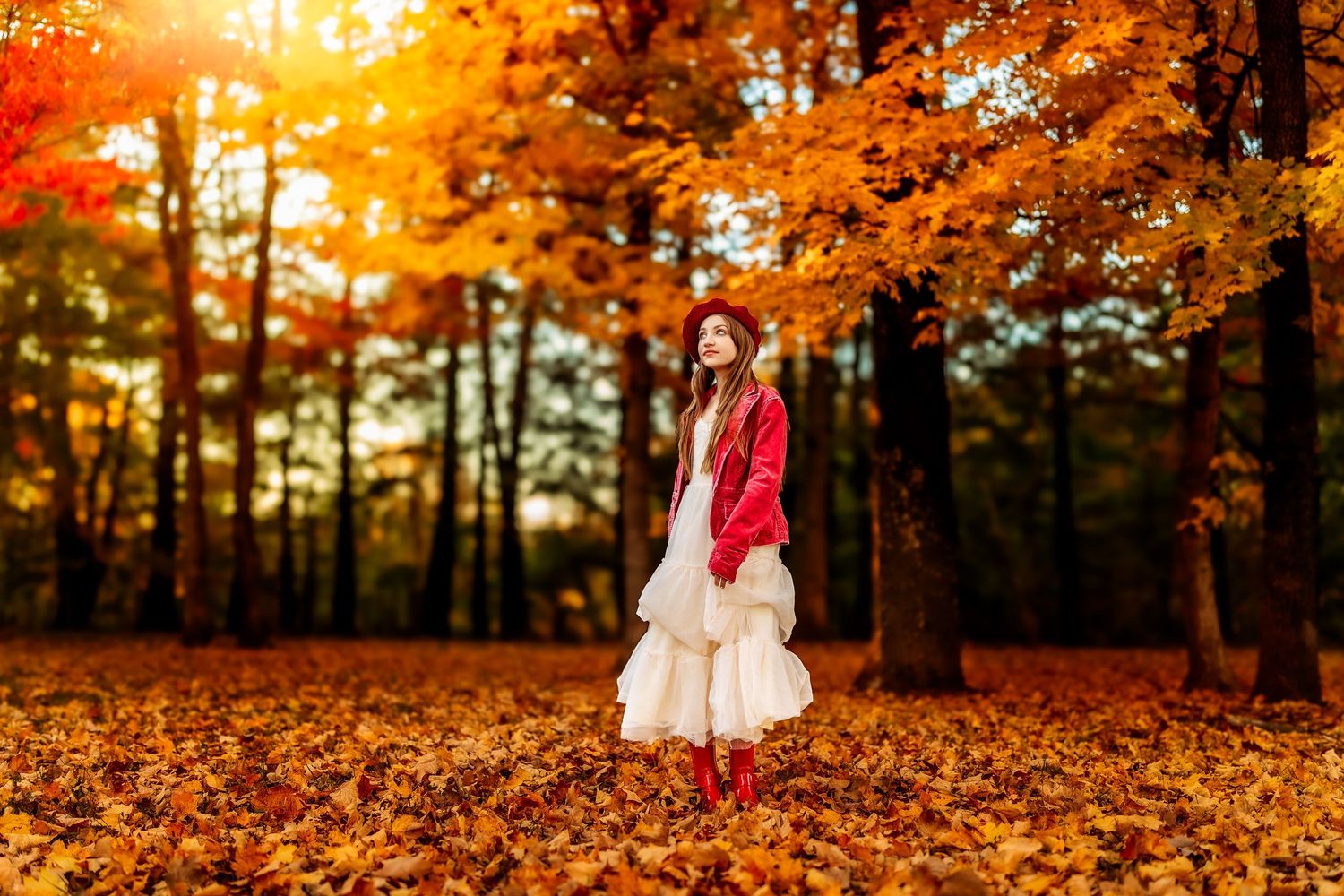 A young woman in a red jacket and white skirt stands among vibrant autumn leaves in a sunlit forest.