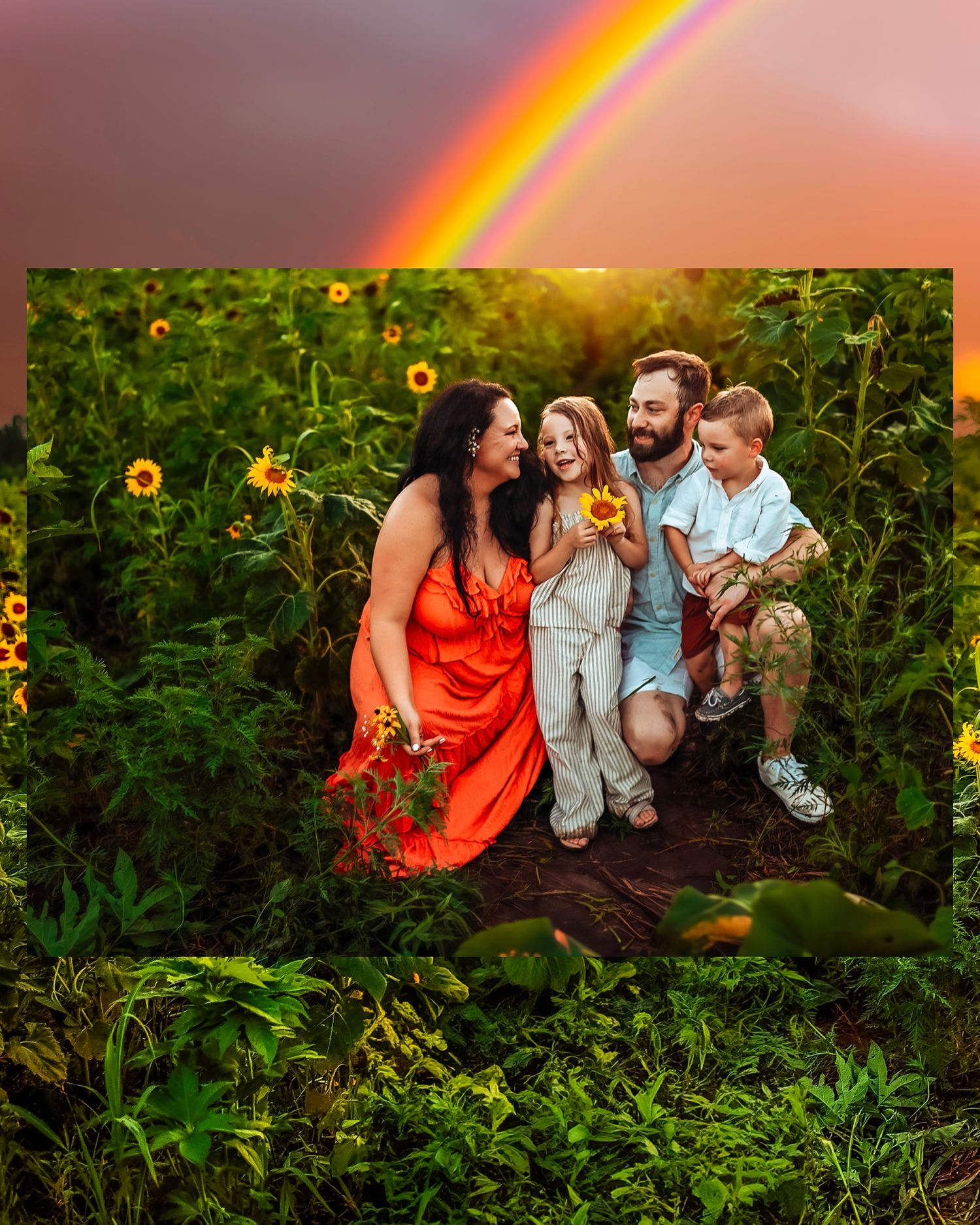 Family of four smiling in a sunflower field with a rainbow in the background, woman in orange dress holding sunflowers.