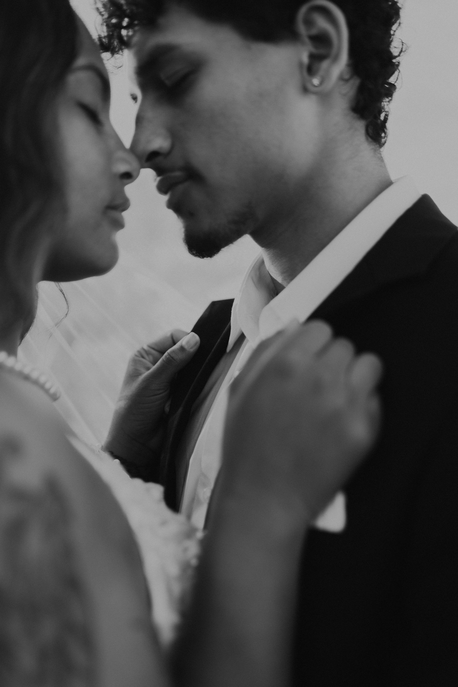 Black and white photo of a couple in wedding attire sharing an intimate moment, nearly kissing.