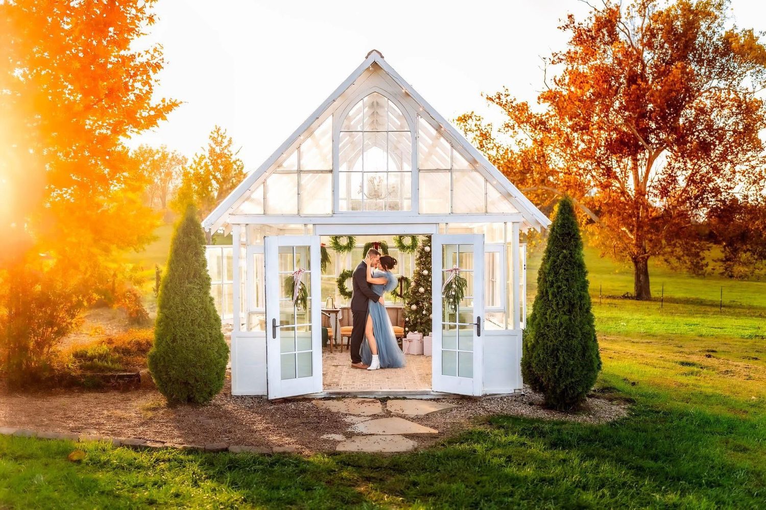 Couple embracing in a white greenhouse chapel surrounded by autumn foliage and golden sunlight.