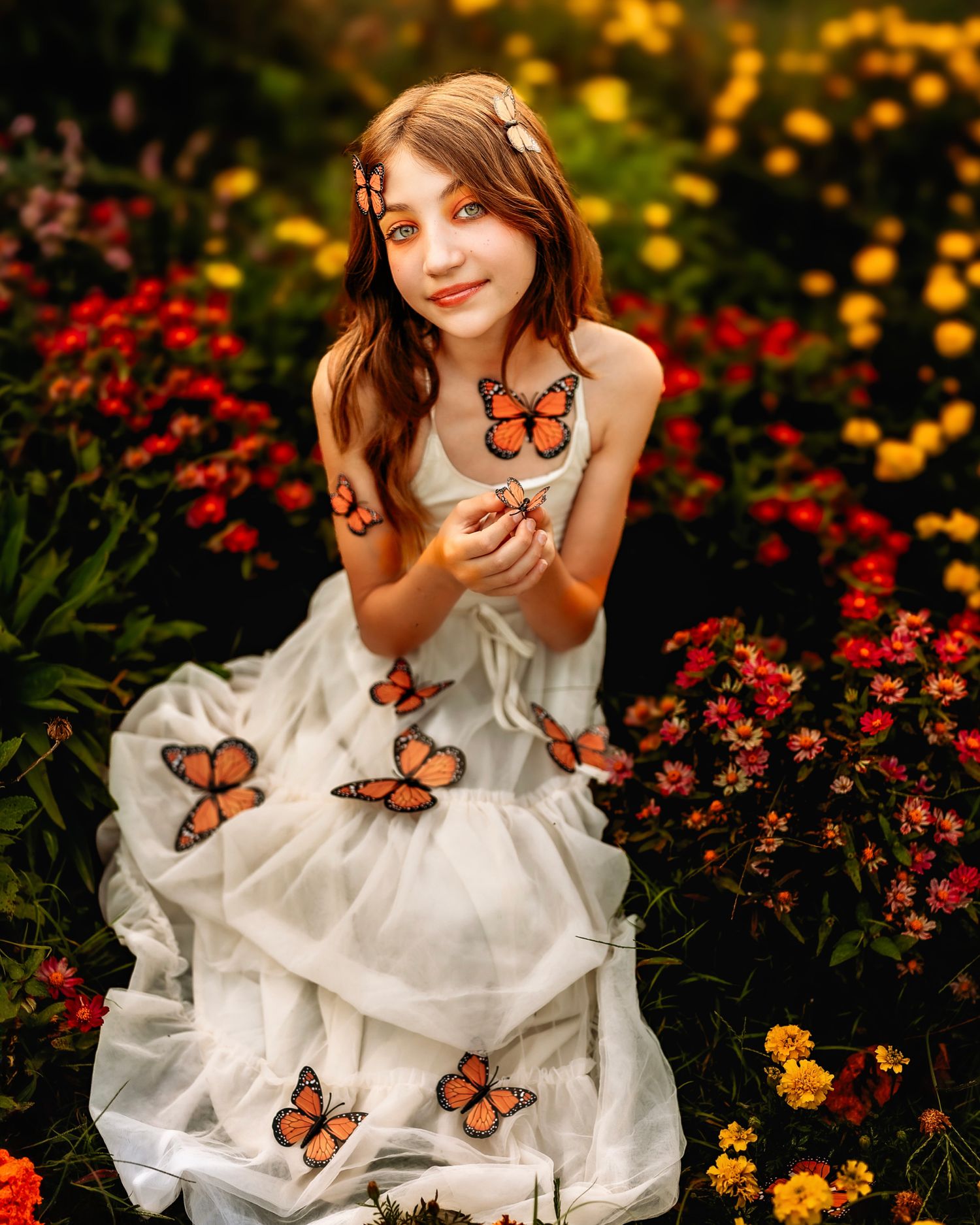 A young girl in a white dress sits among colorful flowers with monarch butterflies resting on her dress and hands.