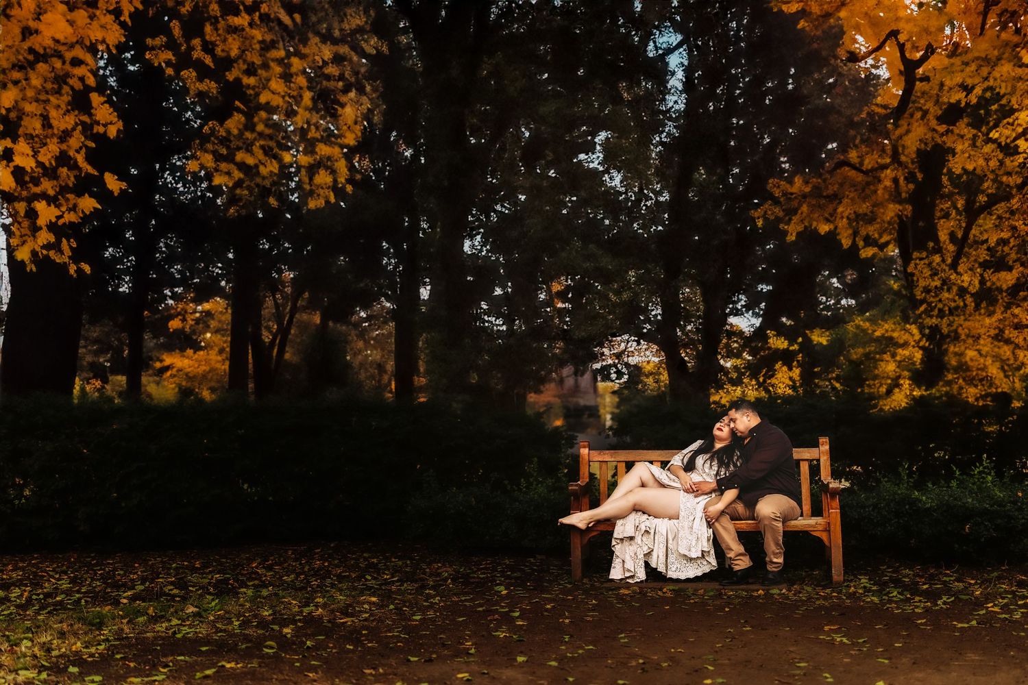 Couple sitting close on a wooden bench in an autumn park surrounded by vibrant orange and yellow foliage.