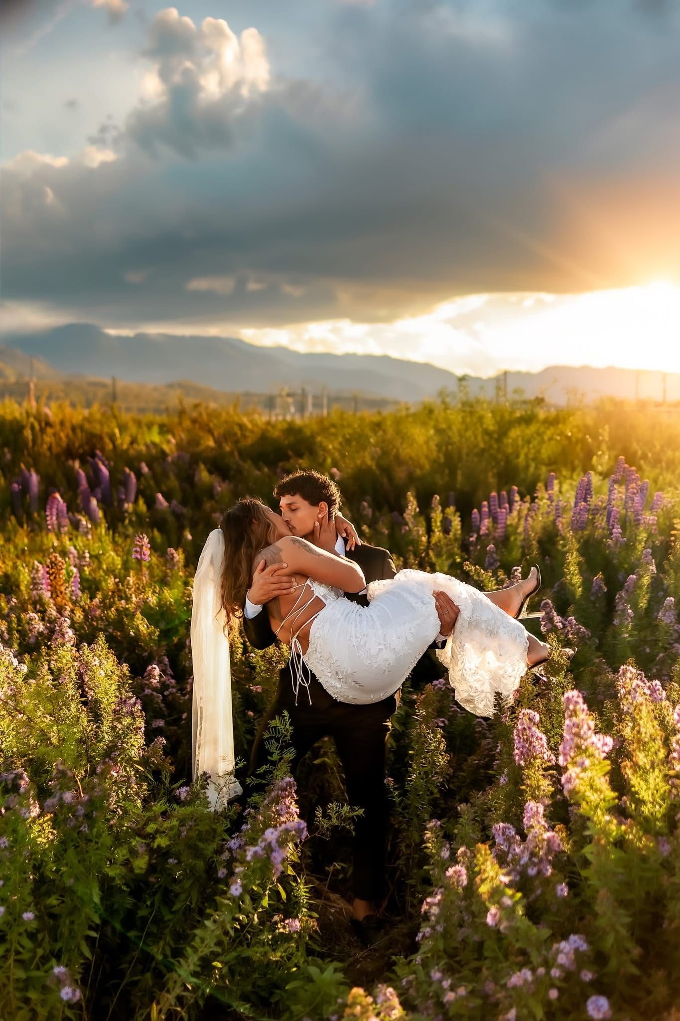 Groom carries bride through a vibrant lupine field at golden hour with mountain views.
