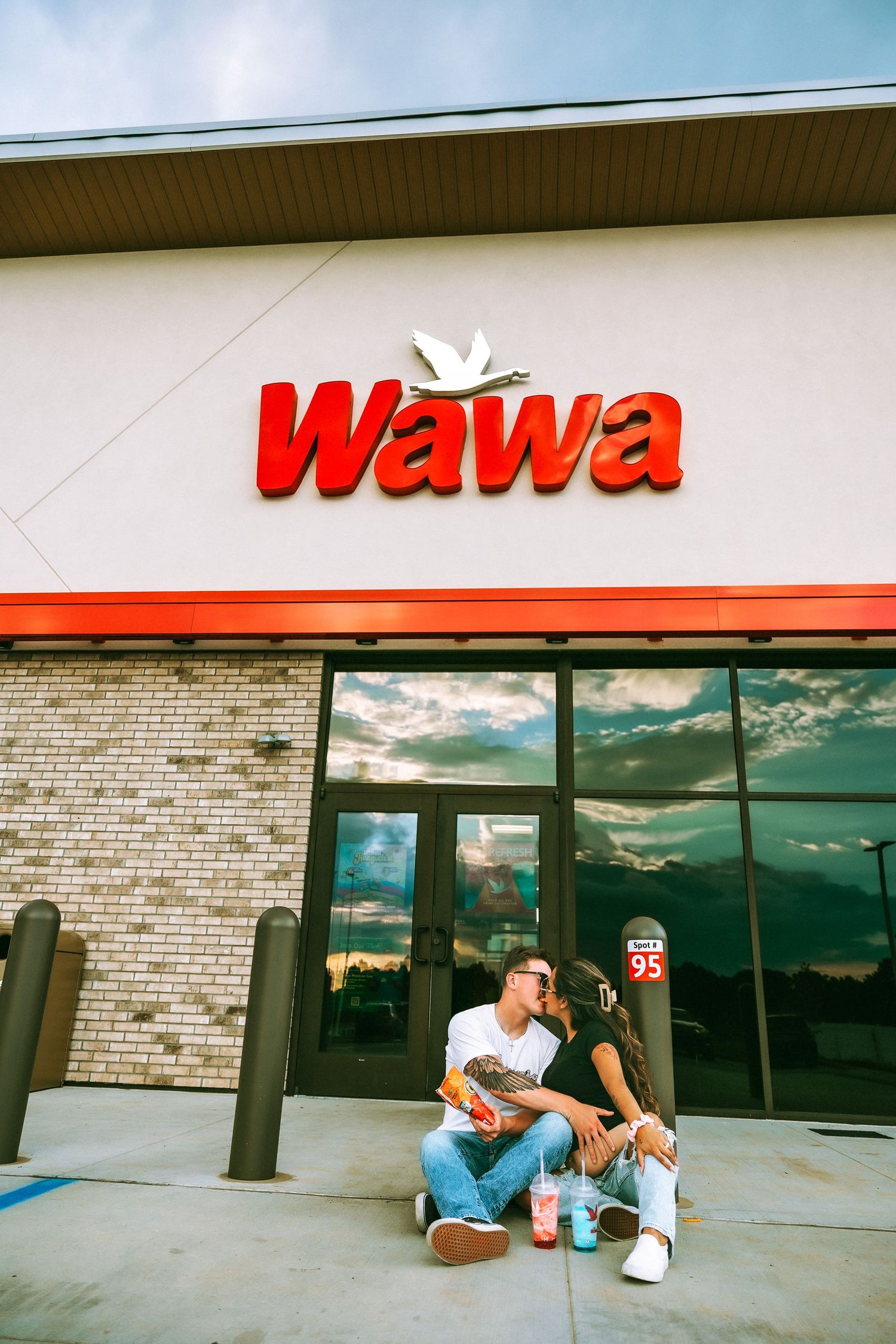 Couple sharing a romantic moment sitting outside a Wawa convenience store entrance under the brand logo.