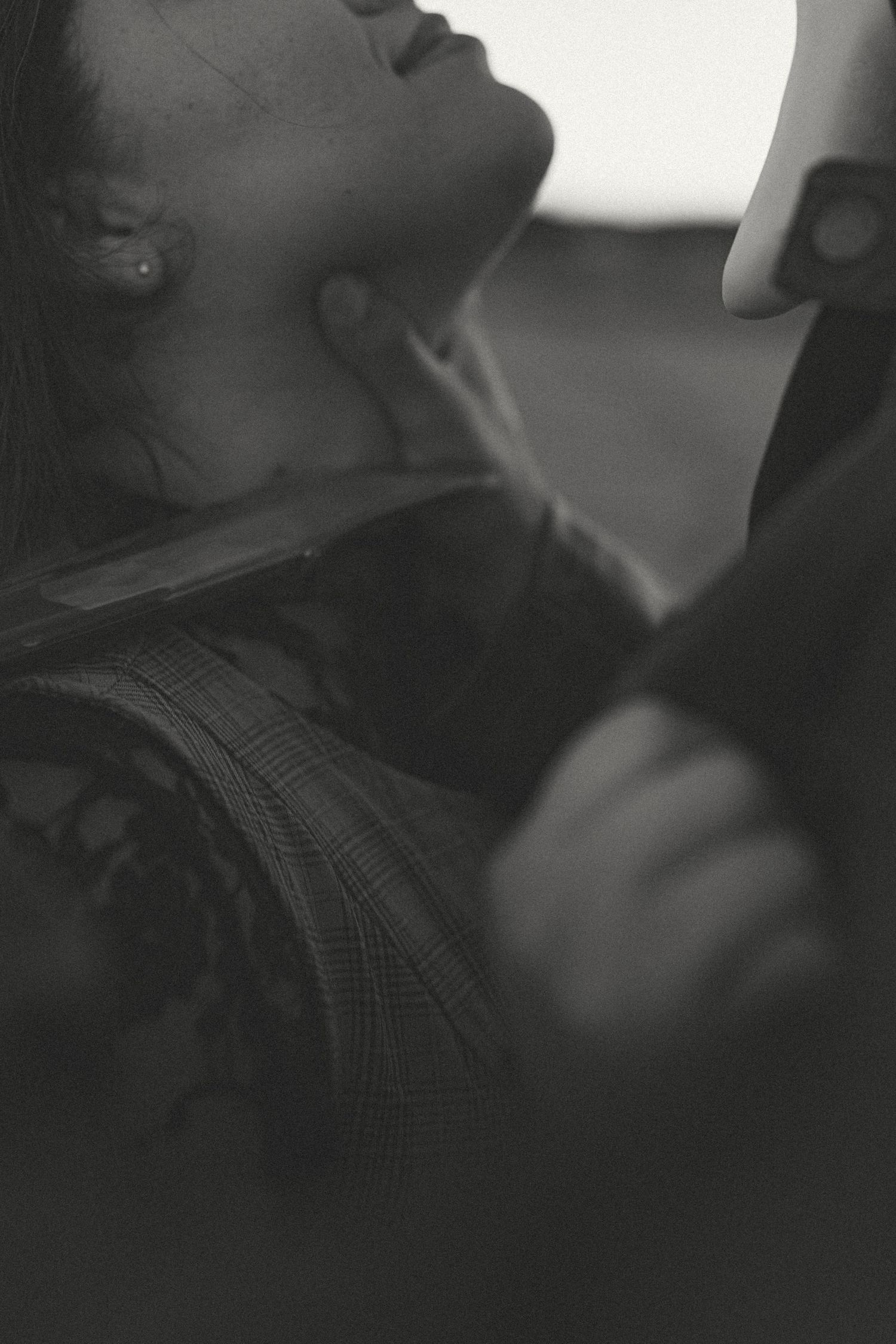 Black and white close-up of a woman with her head tilted back as a hand gently touches her neck, wearing a plaid jacket with lace.