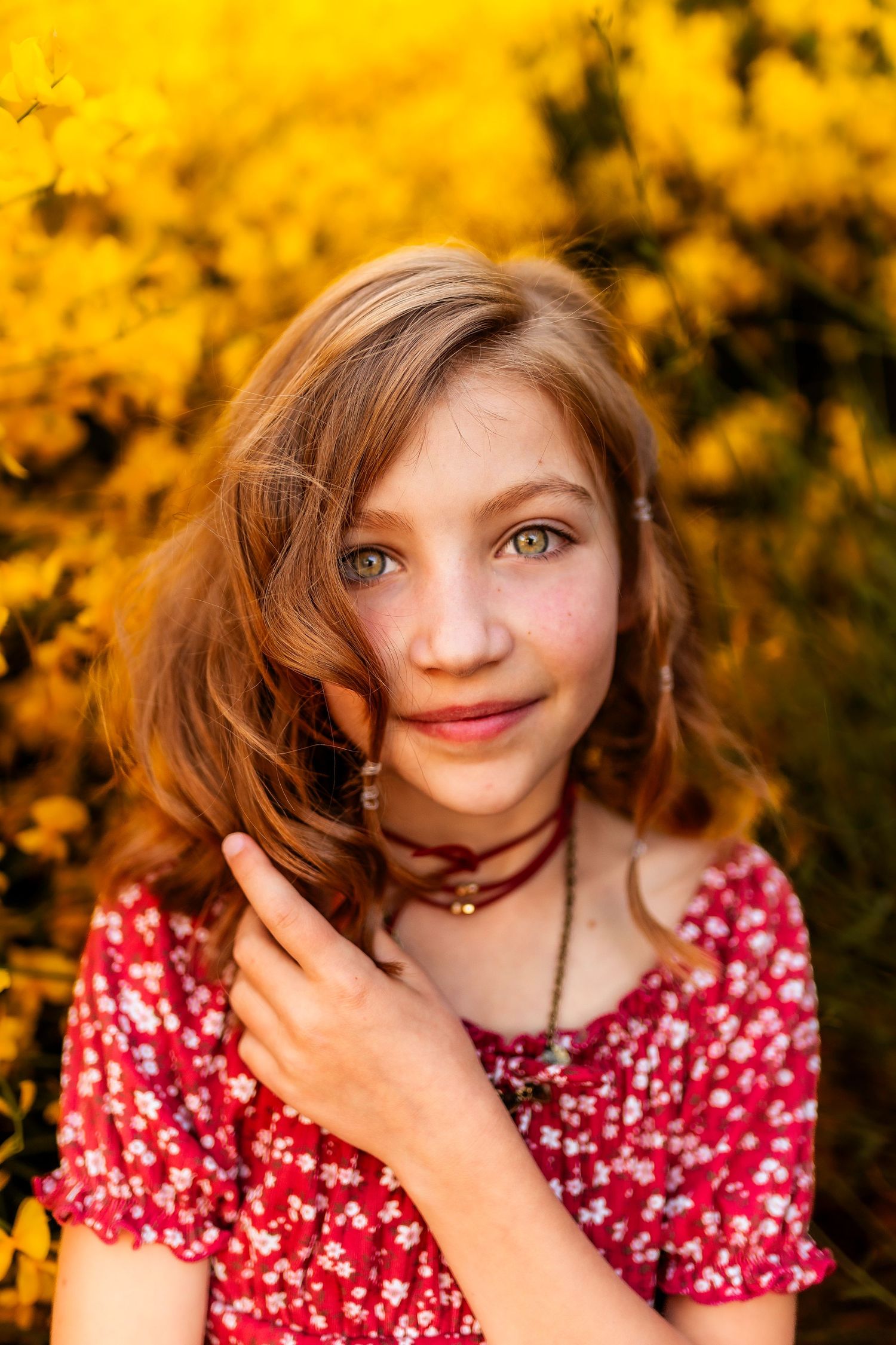 Young girl with green eyes in red floral dress smiling against vibrant yellow autumn foliage backdrop.